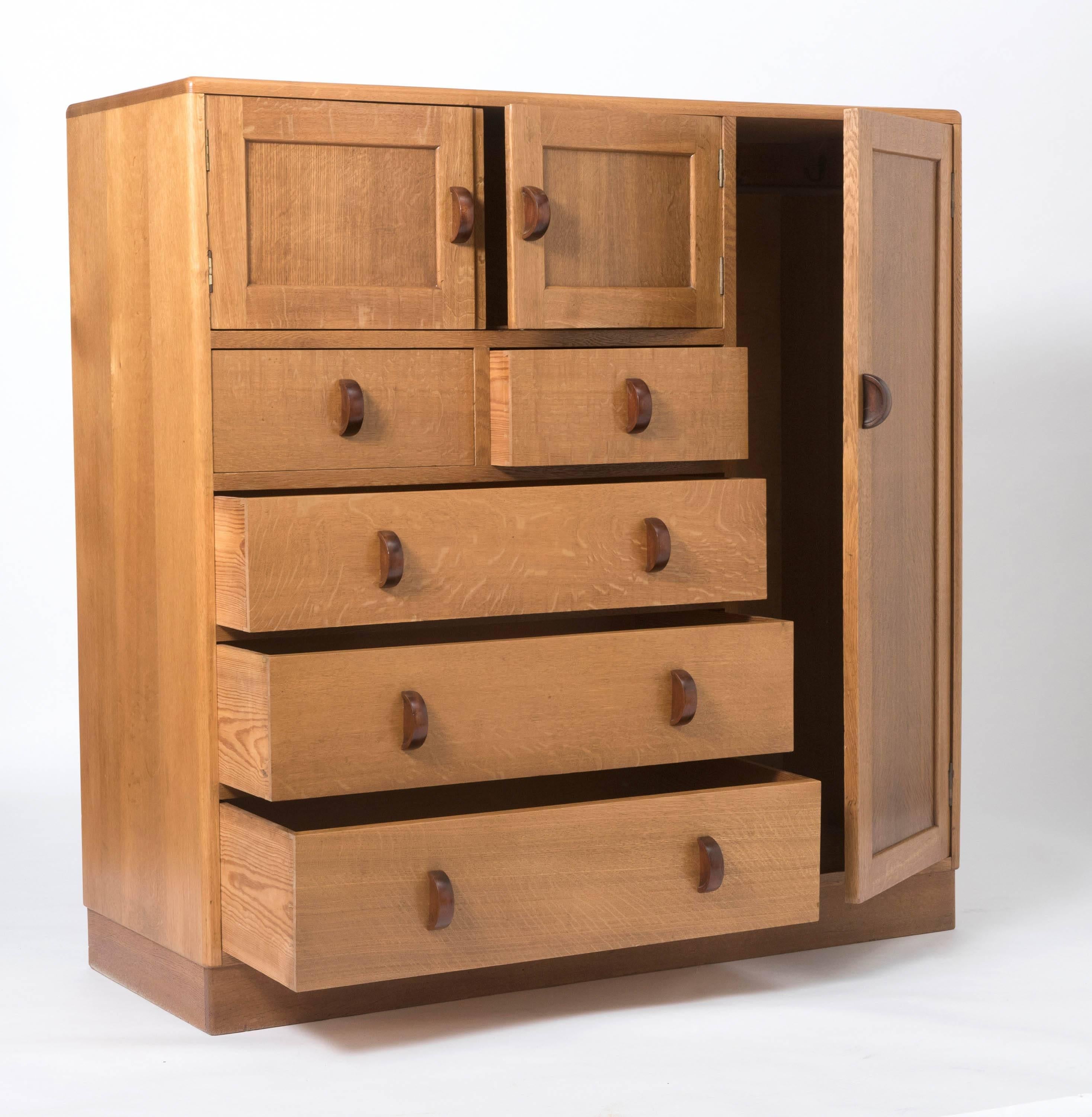 An oak wardrobe compendium by Heals of London.
Ivorine makers disc.
A pair of cupboards over two short and three long drawers.
Flanked to one side by a hanging cupboard.
English, circa 1930.
Measures: 123 cm H x 122 cm W x 46 cm D.
 