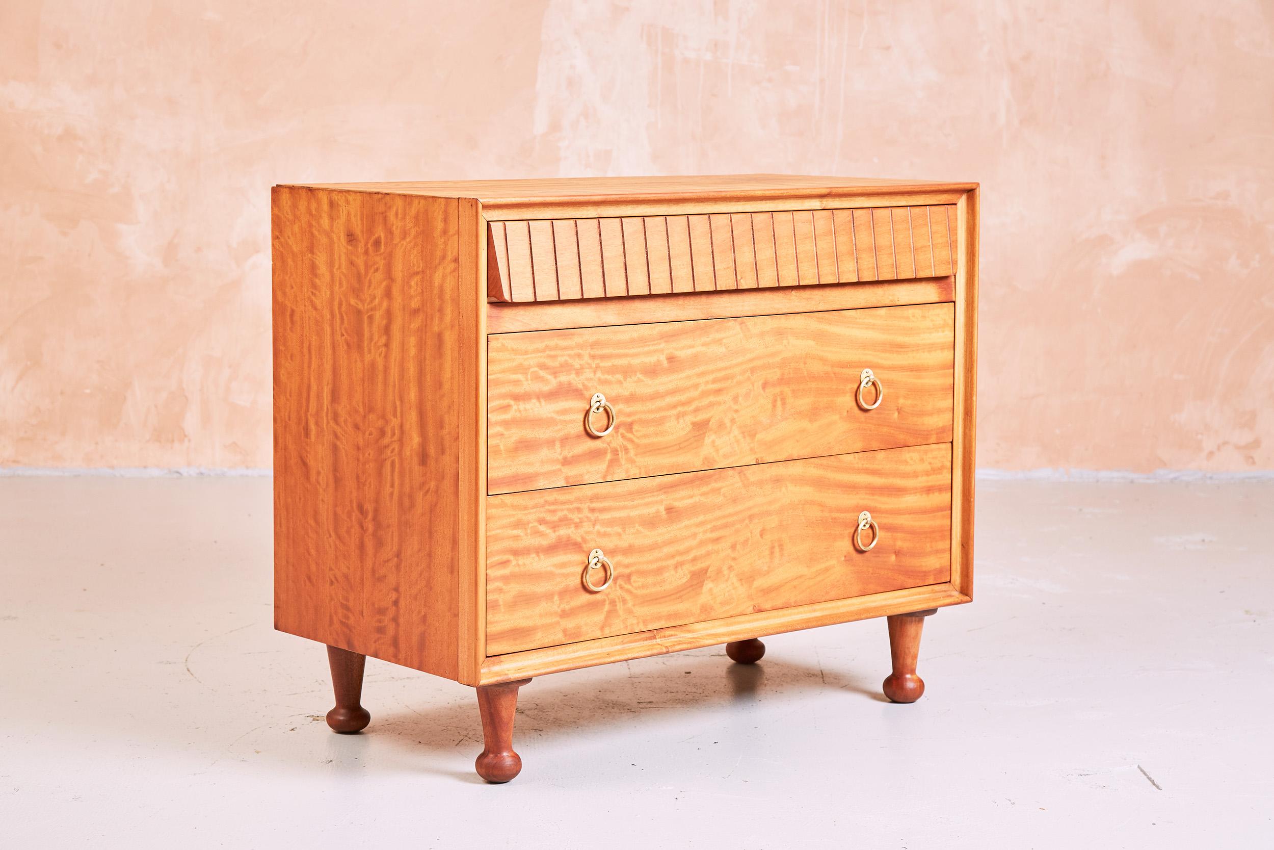 Produced for Heals in the 1950s, this chest of drawers is constructed from Satinwood.
The design is attributed to Andrew Milne.

With three drawers, the uppermost of a fluted design, the chest sits over turned feet.