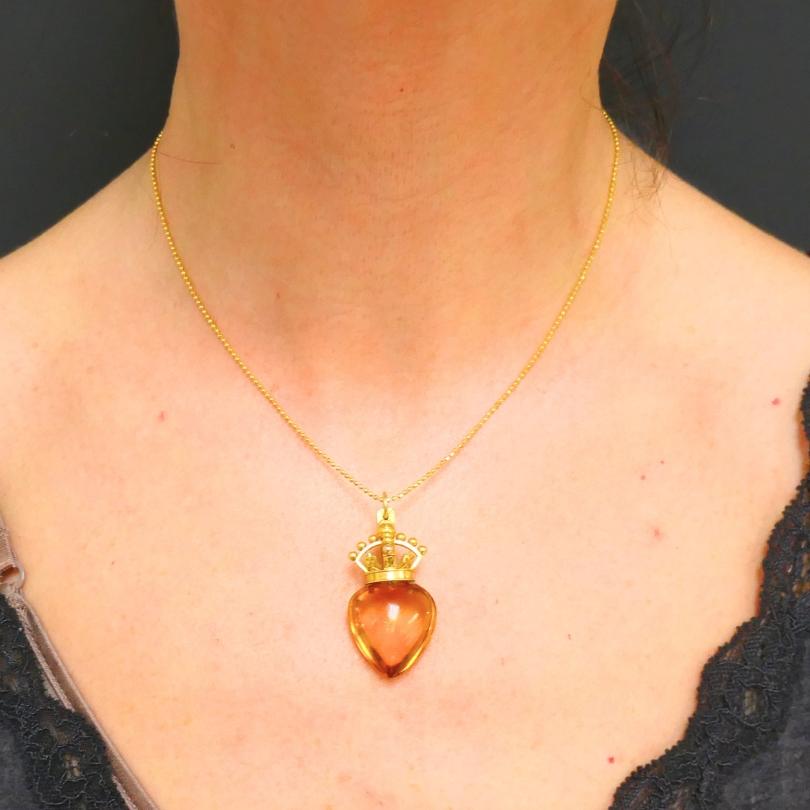 A vintage heart and crown pendant, featuring a heart shaped citrine set in 14k gold. The heart is topped with a small crown, adding a playful touch to the piece. The citrine has a smooth finish that enhances its vibrant yellow hue. The crown above