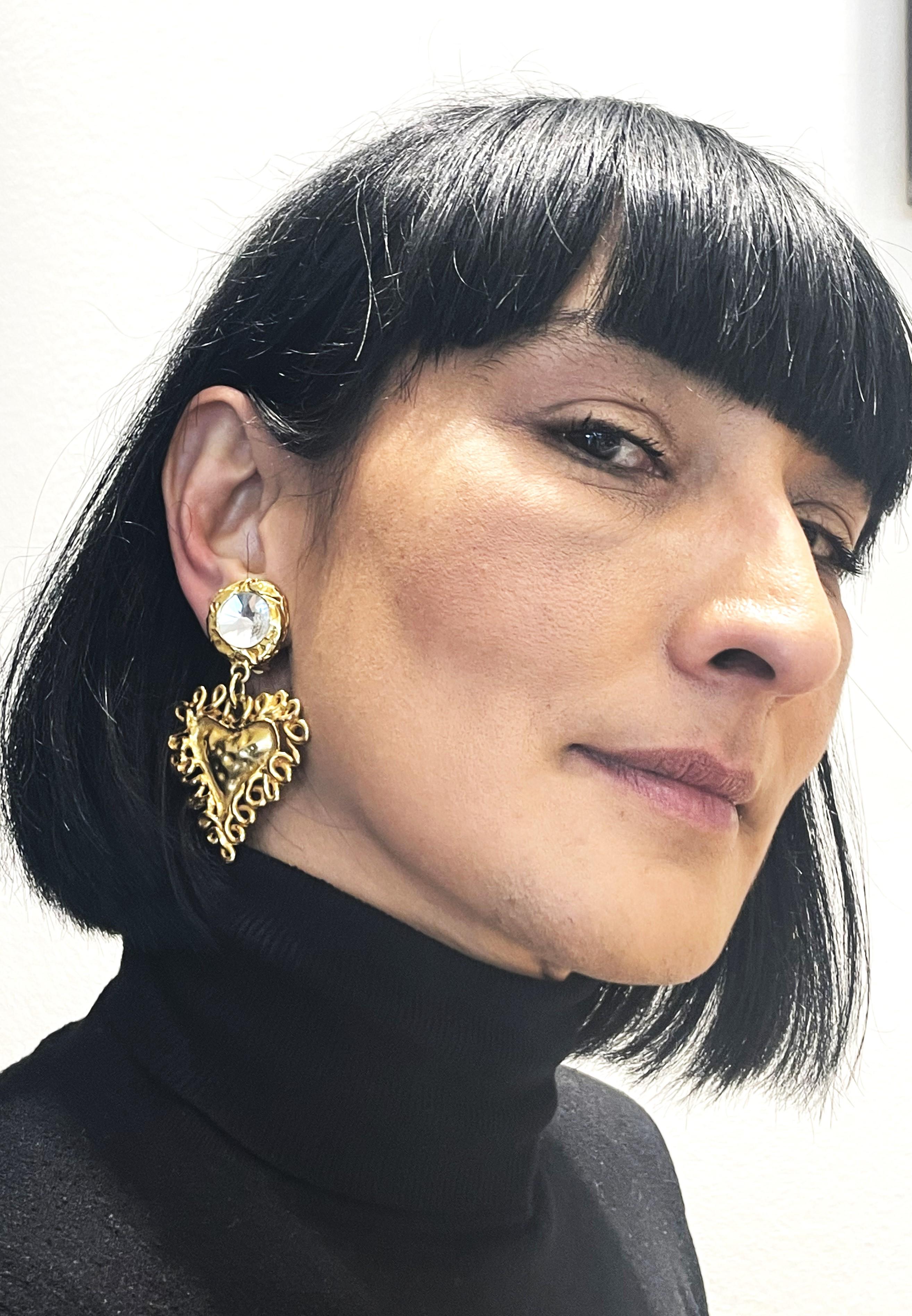 Vintage ear clips signed Christian Lacroix Paris. The upper part consists of a large cut rhinestone with a gold border. Hanging from it is the entwined Lacroix heart. Gold plated, 1980s.

Size: L 7 cm x W 5.5 cm, heart 4 cm x 4 cm, Upper part 2 x 2