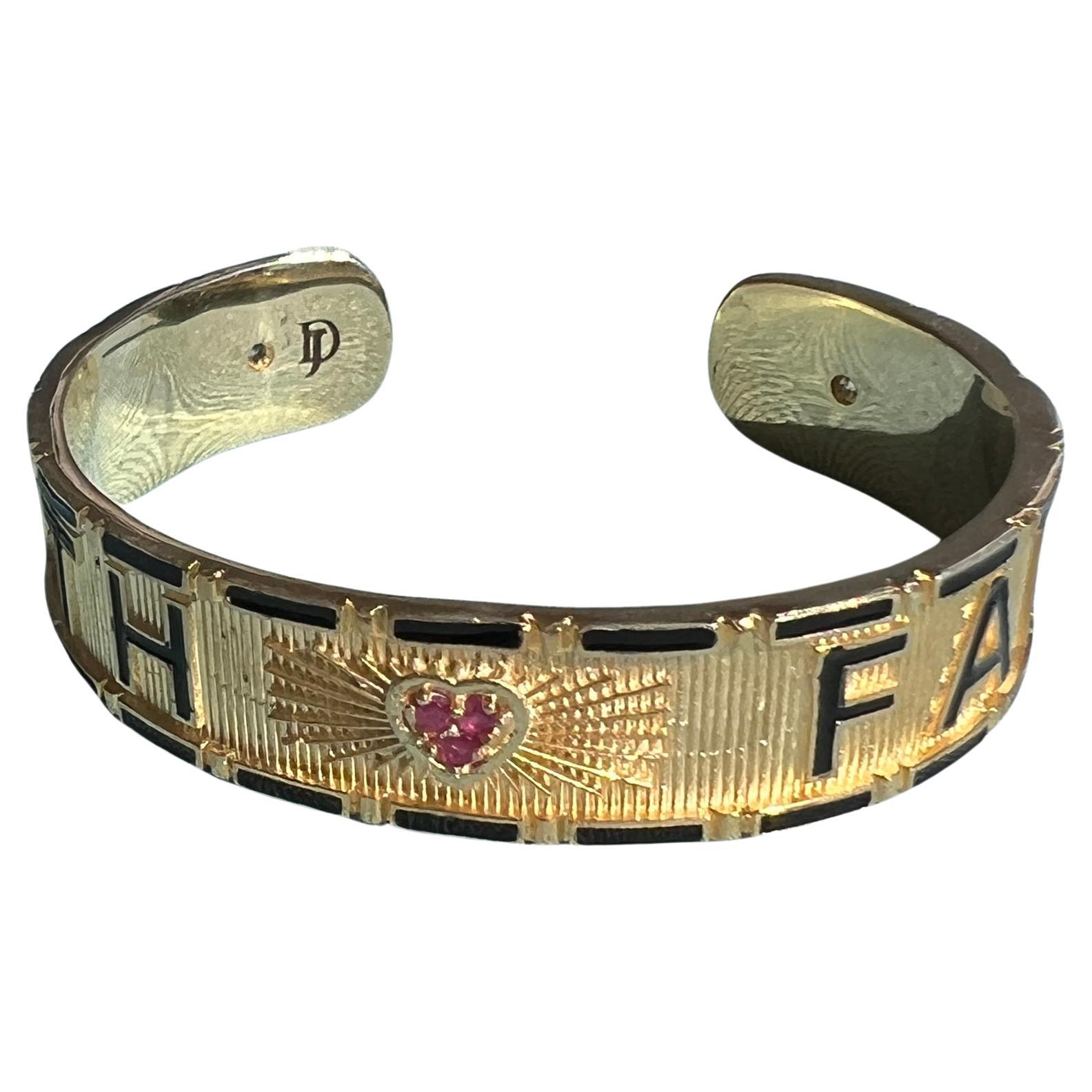 The TRUTH / FAITH cuff bracelet by J Dauphin merges symbolic meaning with sculptural design.
Each side bears an engraved word framed in black enamel — TRUTH and FAITH — balanced around a heart set with three natural rubies and accented by two