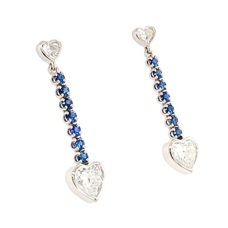 One pair of heart-shaped diamond and sapphire dangling platinum earrings featuring two bezel set, heart brilliant cut diamonds totaling 2.04 ct. (1.02 ct. each) along with two bezel set, heart brilliant cut diamond accents at the top portion