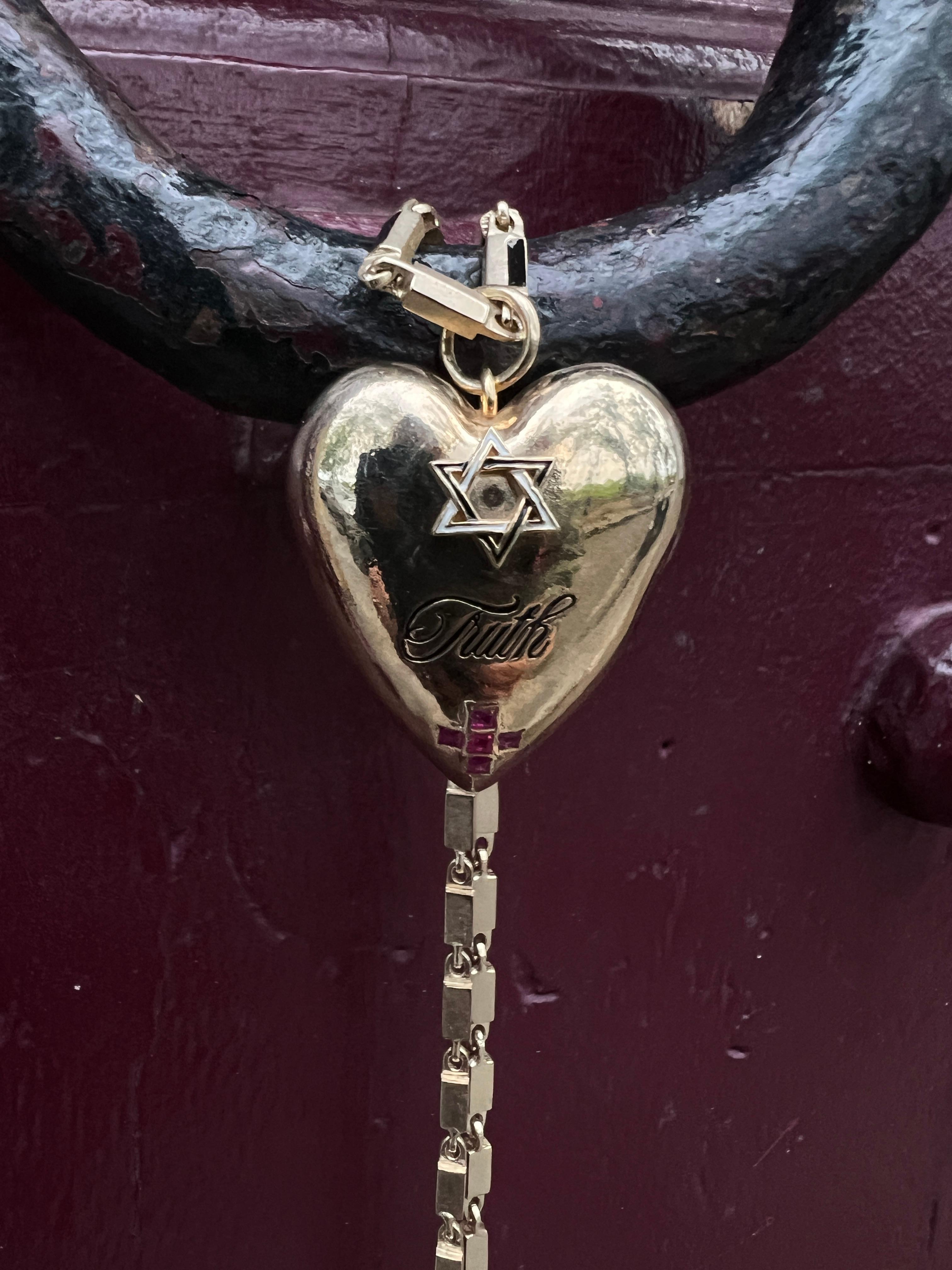 Questa collana simbolica di J DAUPHIN è caratterizzata da un ciondolo a forma di cuore realizzato in ottone placcato oro, con al centro la parola TRUTH. Sopra la parola c'è una stella di David e sotto di essa una croce simmetrica: ogni simbolo è