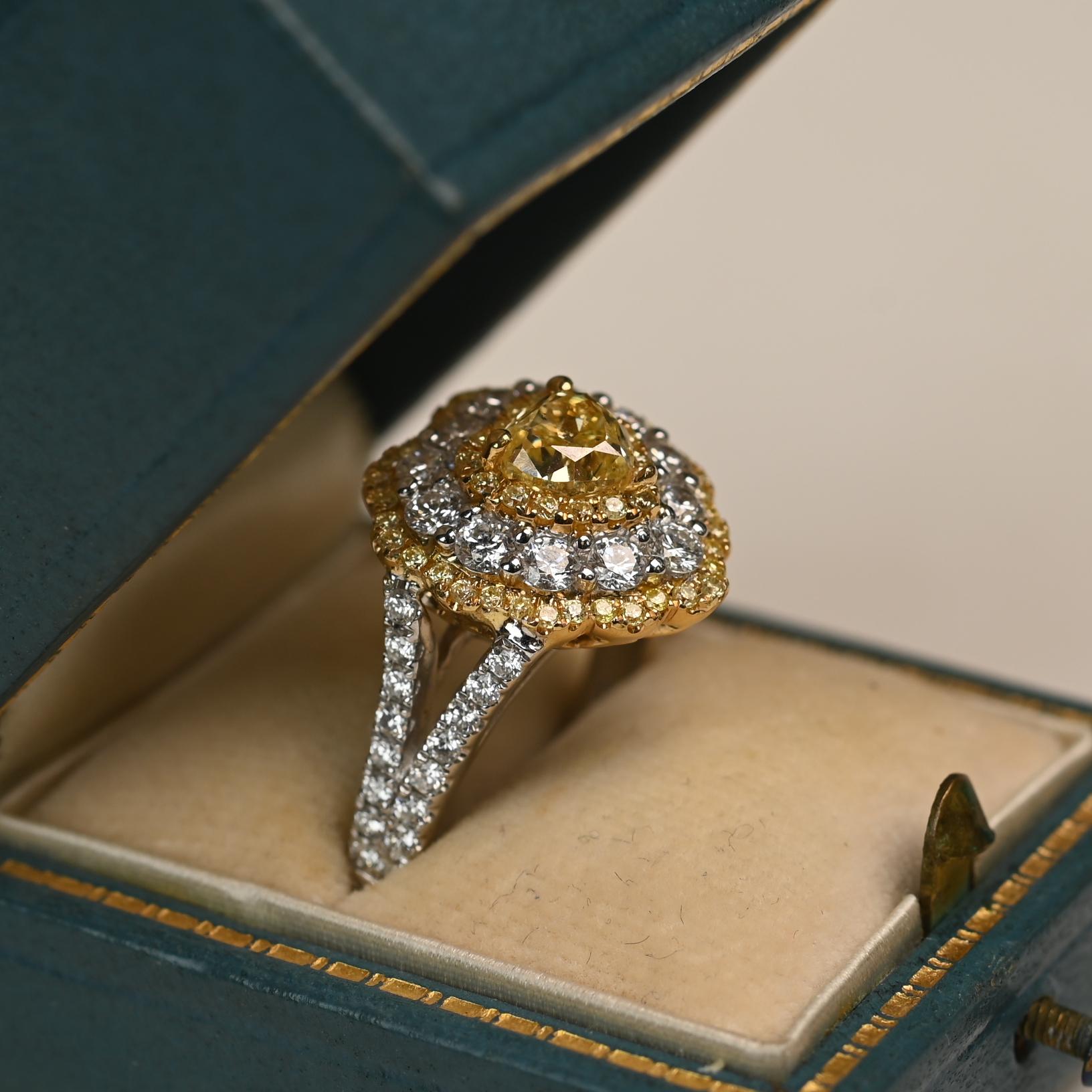 This striking ring showcases an approximately 0.90 carat heart-shaped yellow diamond of SI1 clarity at its center. Surrounding the focal stone are three delicate halos of yellow and white diamonds, enhancing its brilliance and emphasizing the rare
