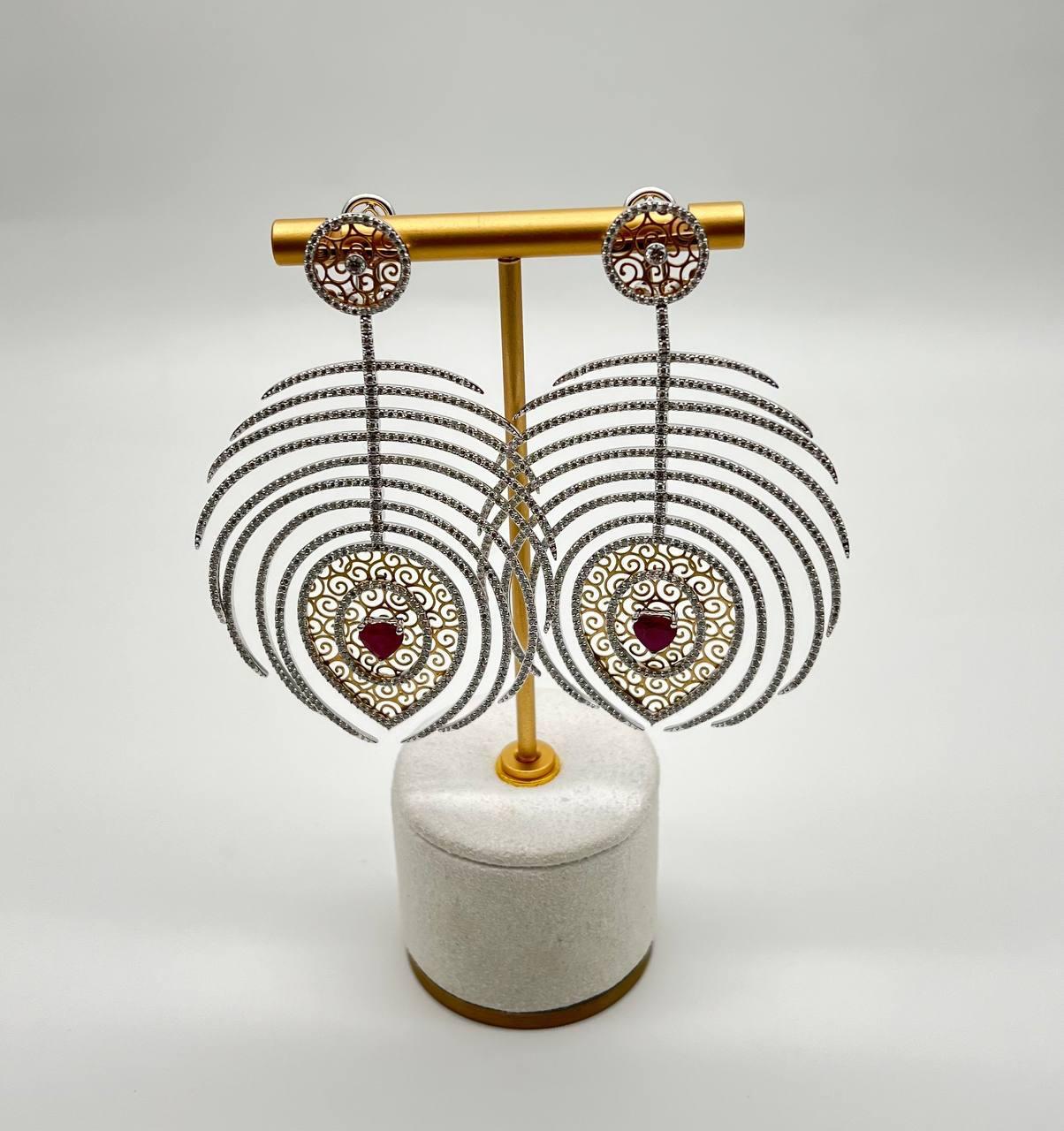 Featuring intricate filigree designs, these earrings are adorned with delicate patterns and a striking central heart-shape red rubies.

The cascading arcs create a mesmerizing silhouette, adding a touch of sophistication.

Crafted with precision,