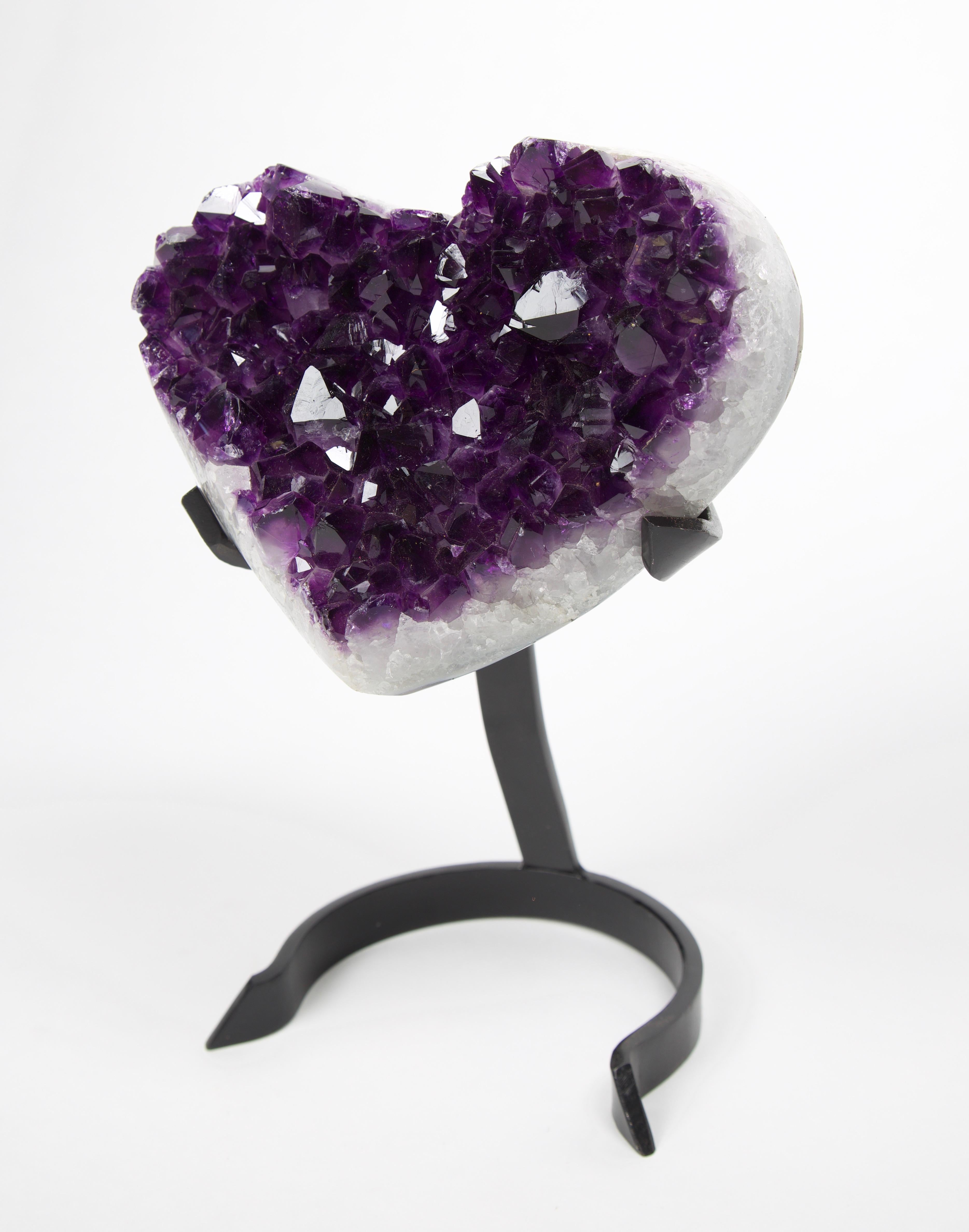 Heart-shaped Amethyst geode on a black metal stand. With polished edges, this amethyst has deep, vibrant violet colors. Local artisans in Uruguay mastered the technique to make heart-shaped gemstones but it's a very labor-intense task that requires