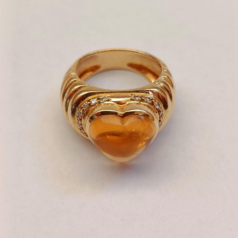 A cocktail ring in 18k yellow gold with a heart-shaped cabochon citrine and brilliant-cut diamonds on the gadrooned shoulder.
France, 1980s-1990s.

Eagle's head French hallmark. Manufacturer's mark unidentified.
Good condition.

Size: US 5 1/2 - UK