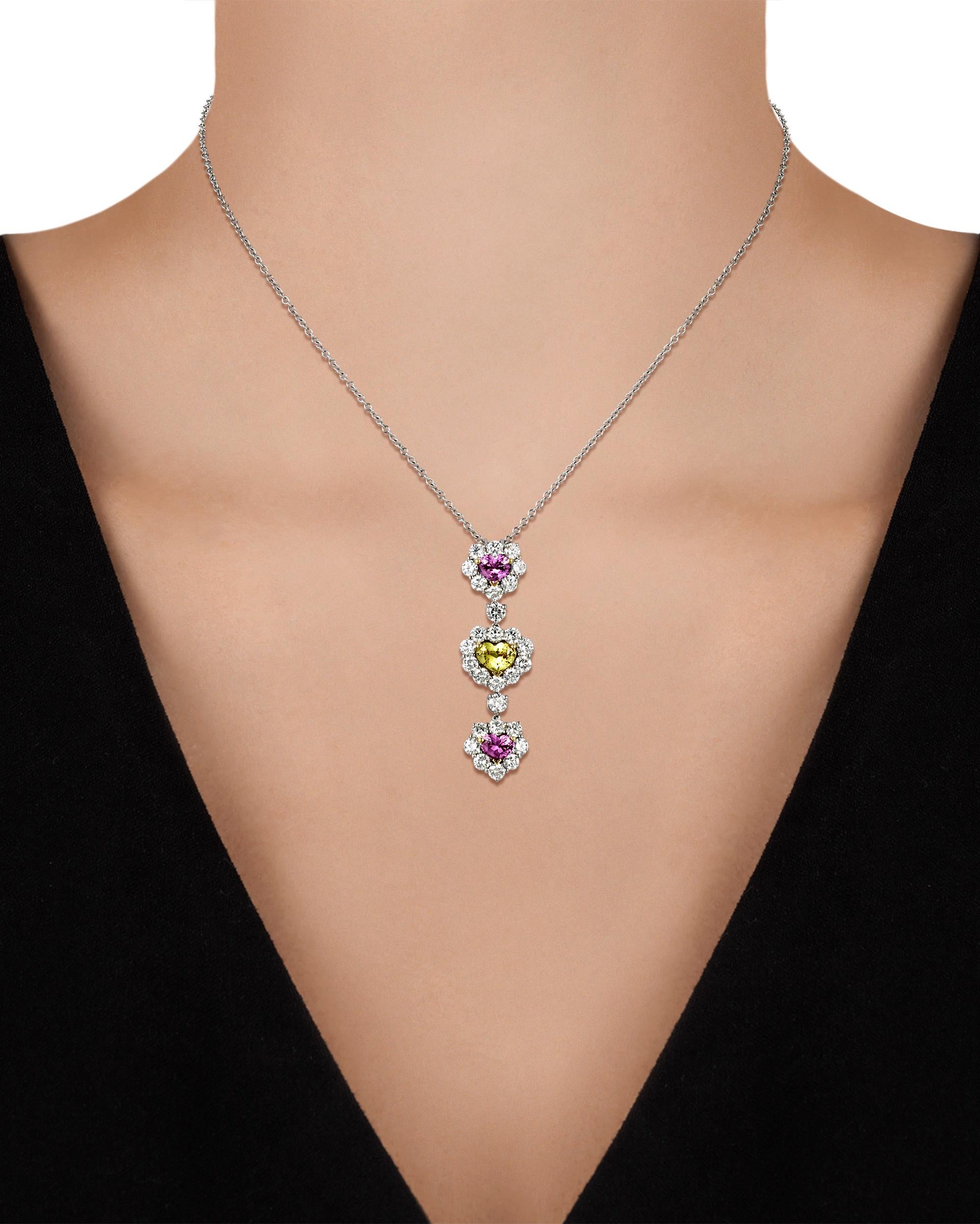 Three heart-shaped fancy colored sapphires weighing a combined 3.20 carats are beautifully set in this charming pendant necklace. Displaying pink and yellow hues, the mixed-cut gemstones have been certified by C. Dunaigre of Switzerland to be