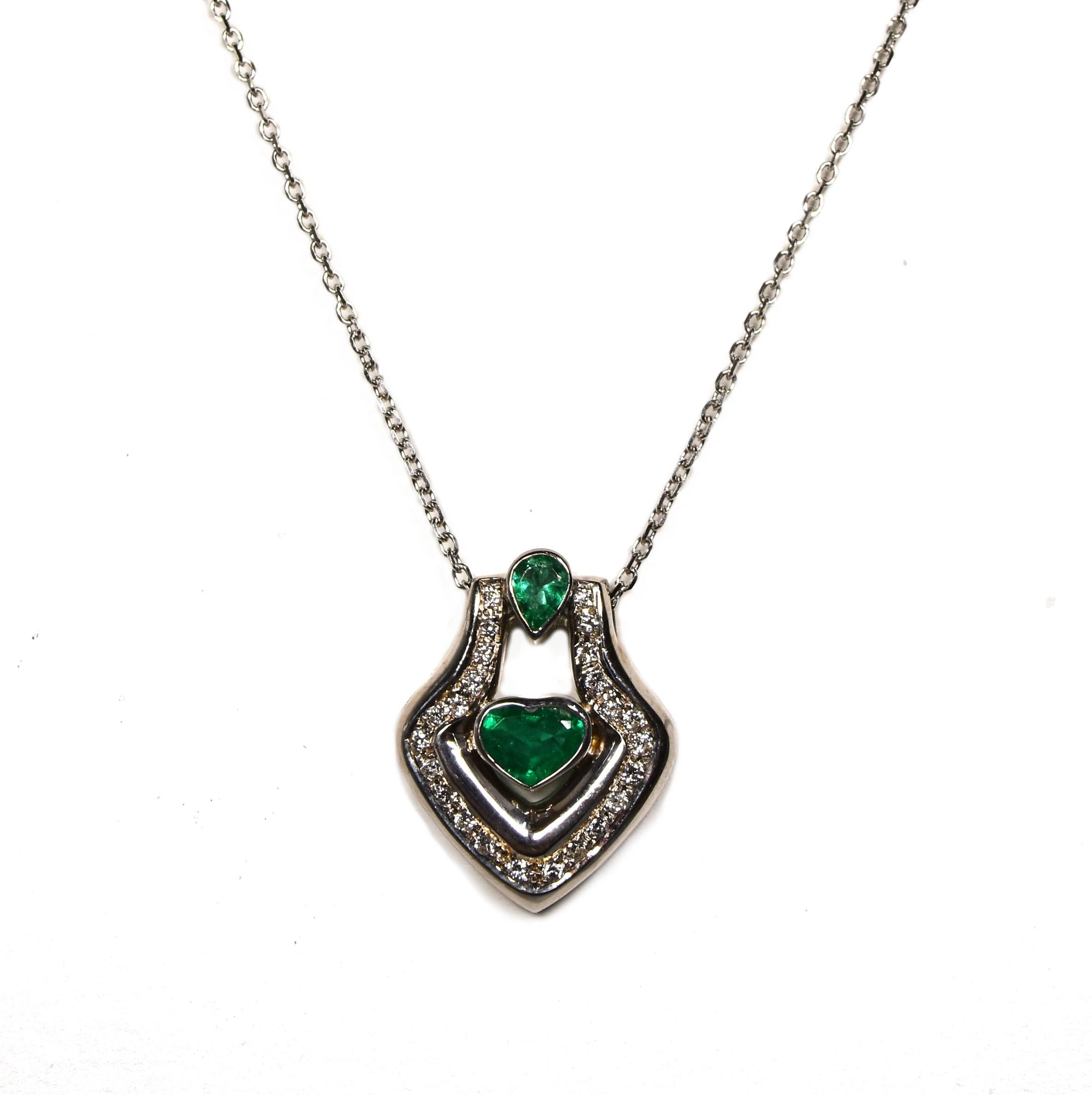 Beautiful pendant set in 18k White Gold which perfectly accents the vibrant hue of the Heart and Pear shaped emeralds in the center of the piece, themselves magnified by a row of pretty and dazzling diamonds. 

A very nice piece with a vintage