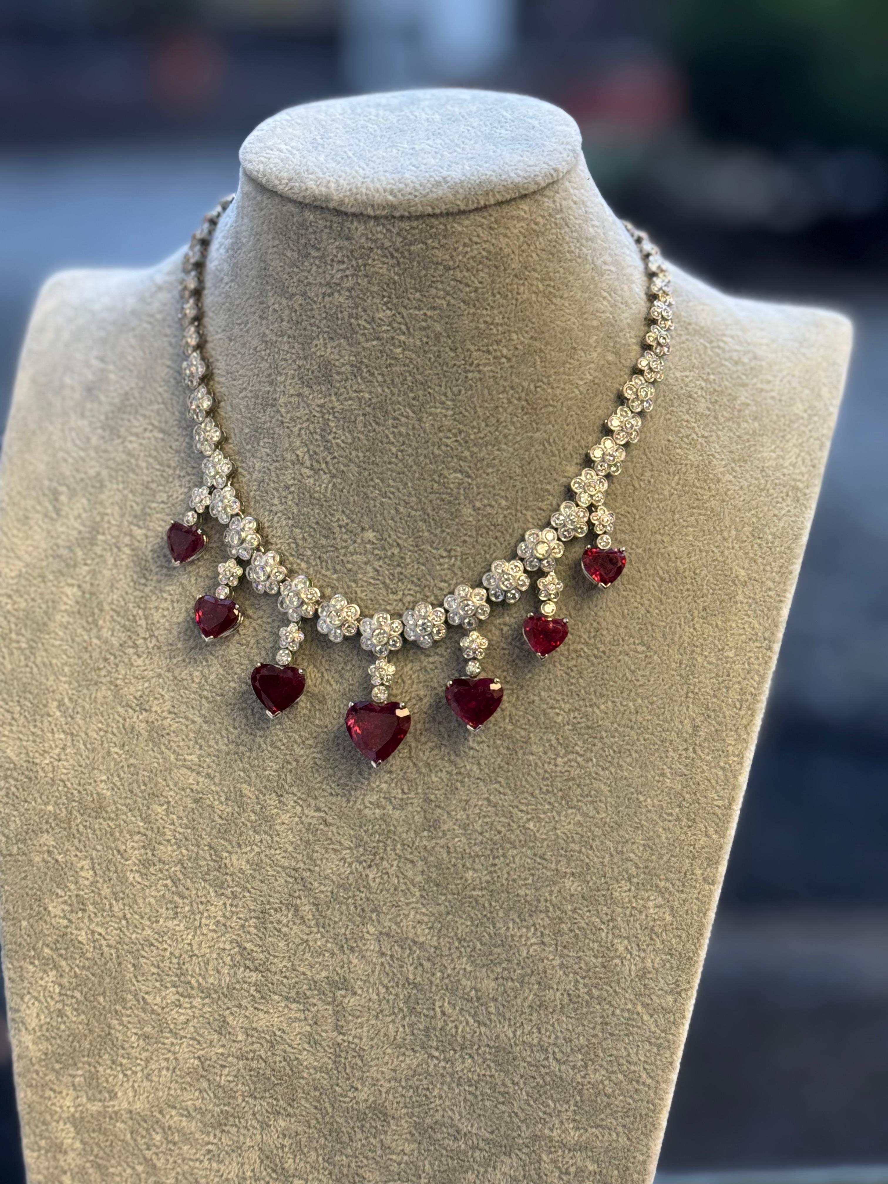 A breathtaking platinum necklace designed with a romantic floral motif, featuring seven vibrant heart-shaped rubellite tourmalines totaling approximately 34.19 carats. Each drop is suspended from a cascade of platinum-set brilliant-cut diamonds—359