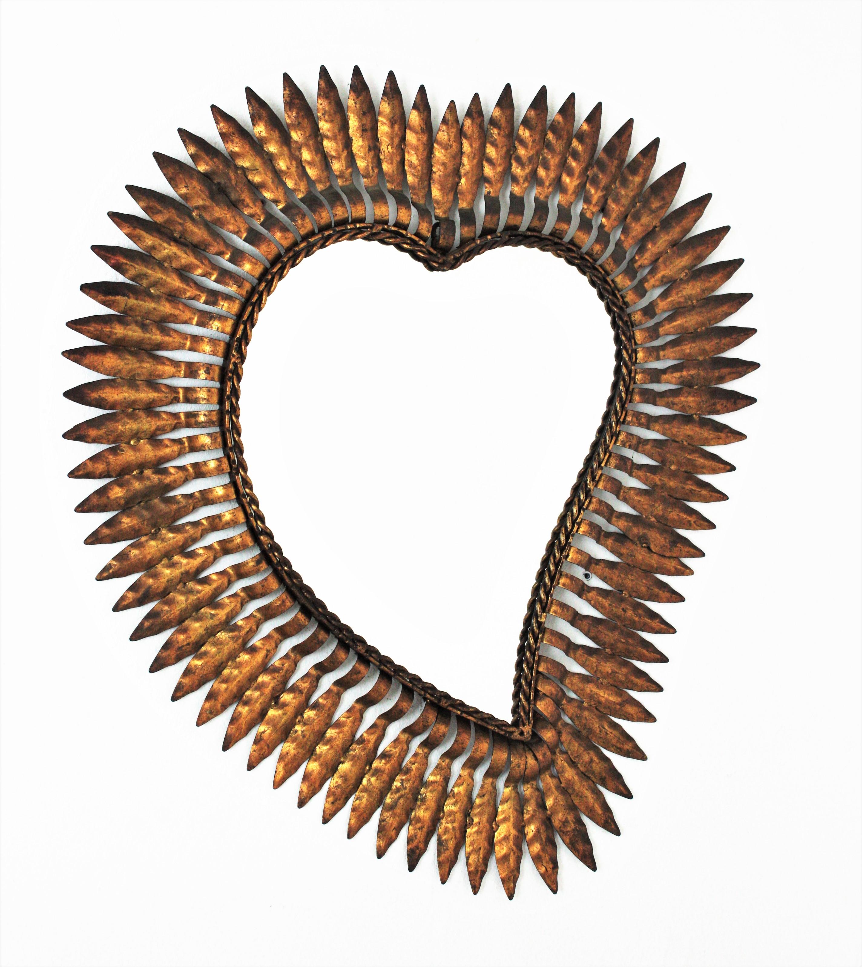 Mid-Century Modern wrought iron sunburst heart shaped wall mirror with gold leaf finish, Spain, 1950s.
This highly decorative sunburst gilt iron mirror has a nice color and a terrific aged patina showing its original gold leaf gilding.
Unusual