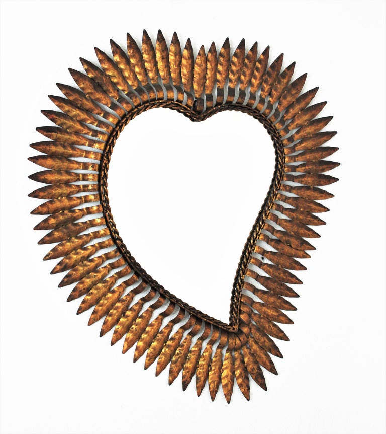 Mid-Century Modern wrought iron sunburst heart shaped wall mirror with gold leaf finish, Spain, 1950s.
This highly decorative sunburst gilt iron mirror has a nice color and a terrific aged patina showing its original gold leaf gilding.
Unusual