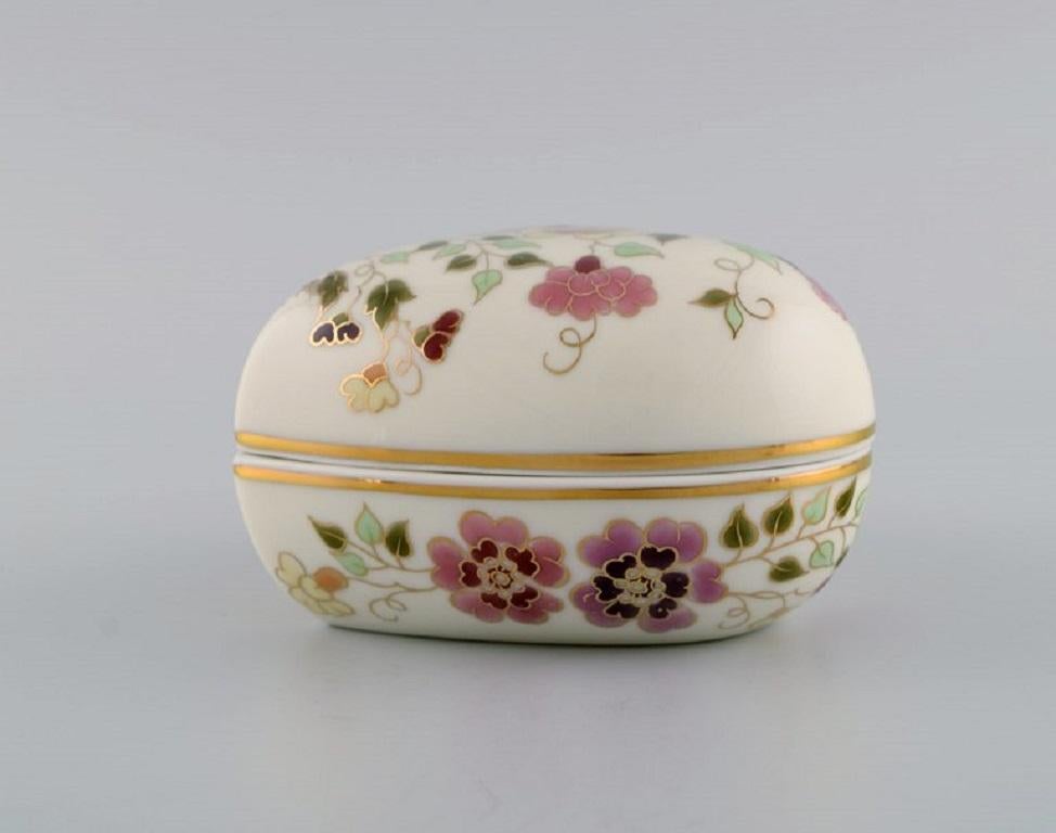 Boîte à couvercle Zsolnay en forme de cœur, en porcelaine couleur crème, avec fleurs, papillons et décorations dorées peintes à la main. 
Fin du 20e siècle.
Mesures : 12 x 6,5 cm.
En parfait état.
Estampillé.