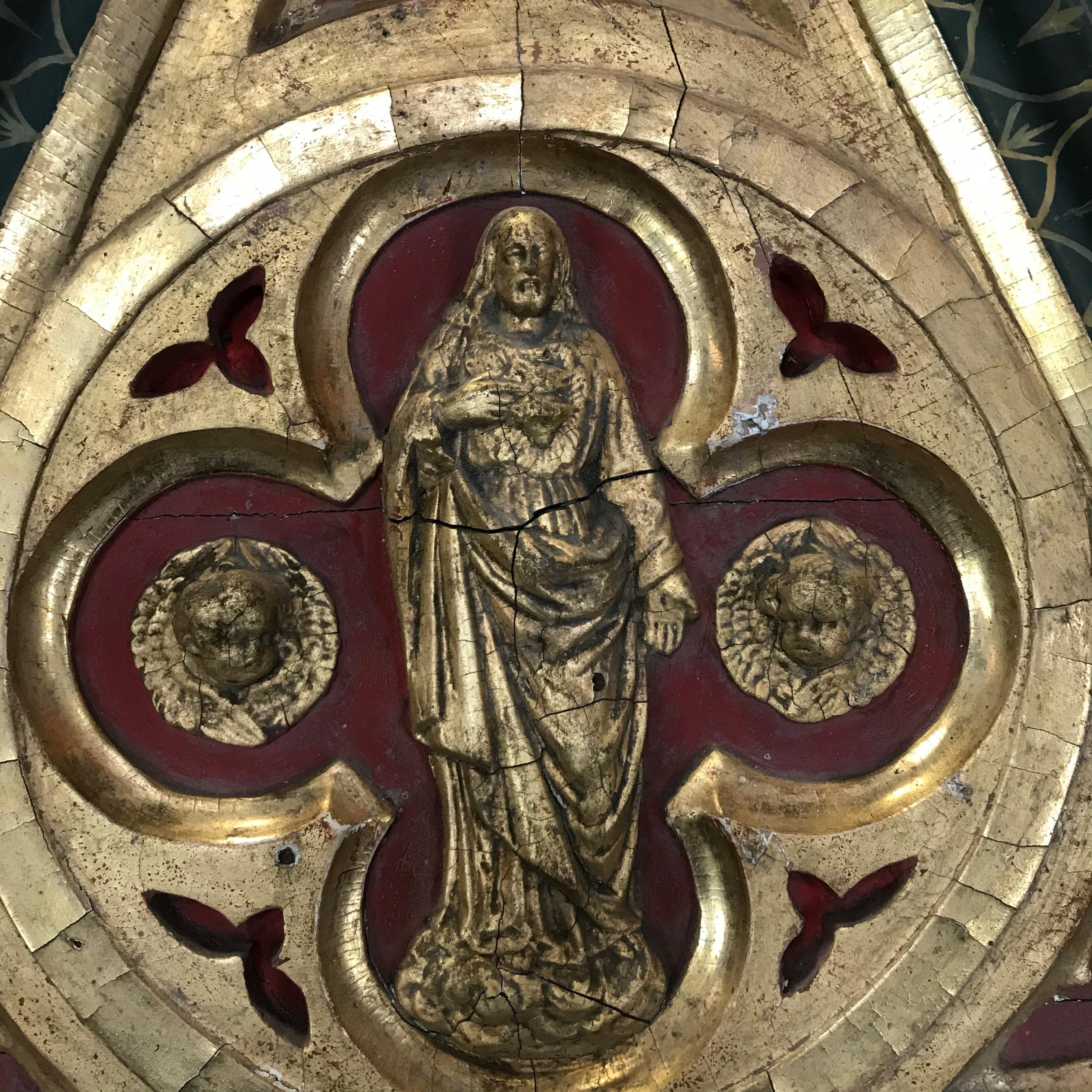 Un incredibile pezzo d'arte da parete estratto da una chiesa francese del XIX secolo. La scultura da parete ha una forma gotica con legno dorato intagliato e un bellissimo bassorilievo dipinto nella parte superiore di un santo con cherubini. La