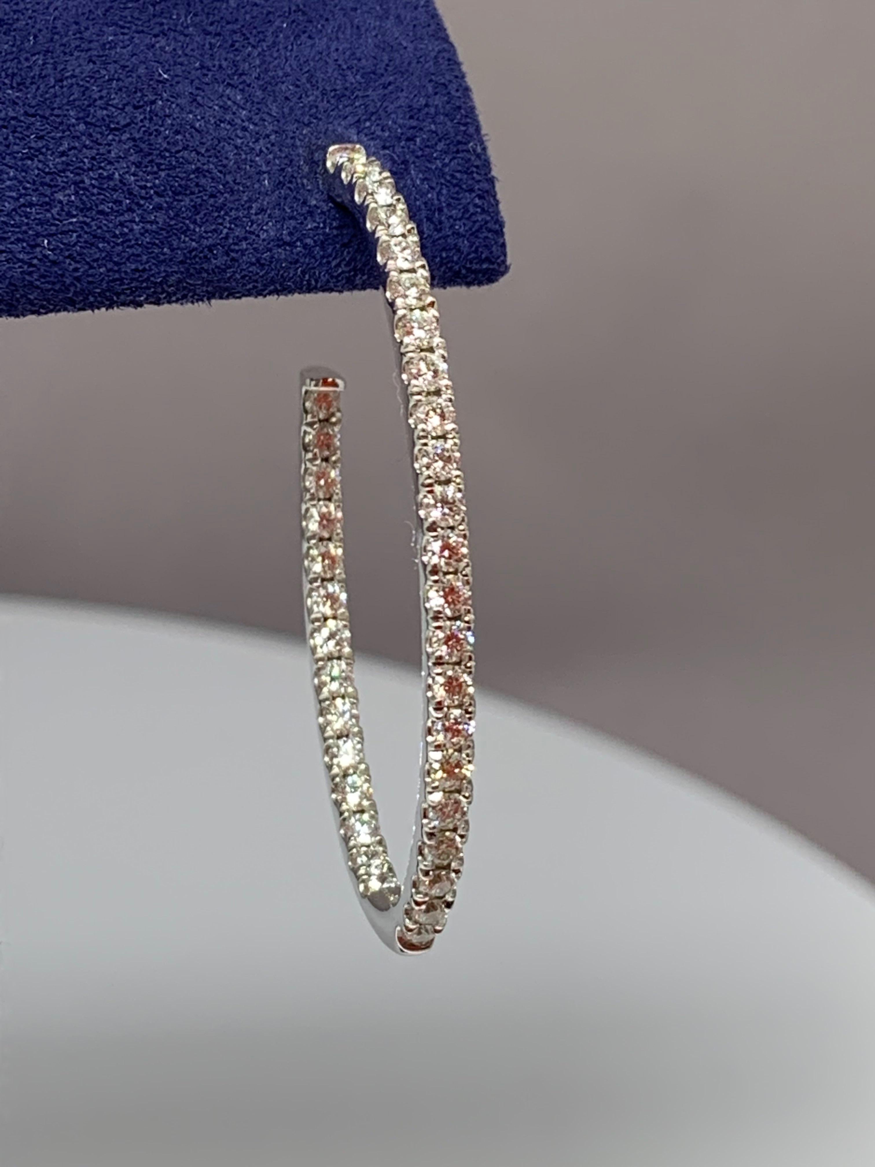 These classic Hearts On Fire diamond oval-shaped hoop earrings feature a total round diamond weight of 1.97 carats and are made of 18K white gold. The earrings are inside-outside prong-set diamond hoops and include sturdy tension backs. These