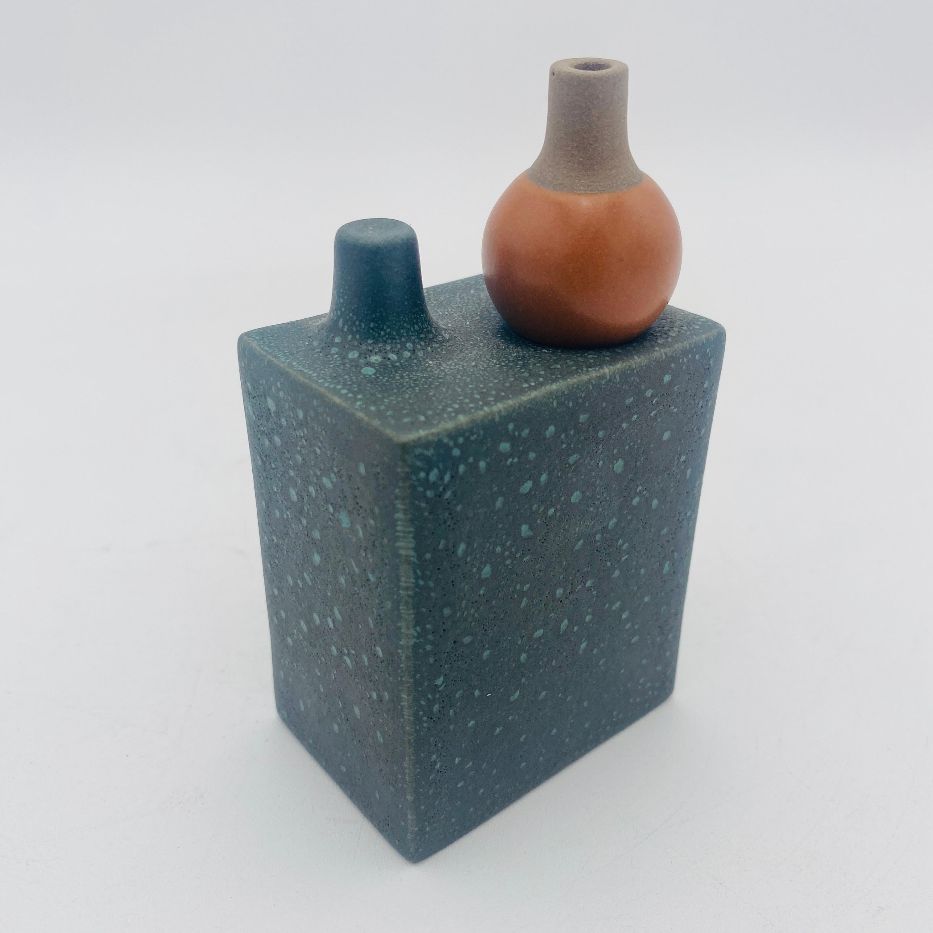 A mini-vase in two parts — box and stopper — intersects art and function to push the limits of a functional vessel. In Basalt over KPFA Green and Persimmon, it is a textured sculptural piece of art unto itself, yet transforms for playful floral