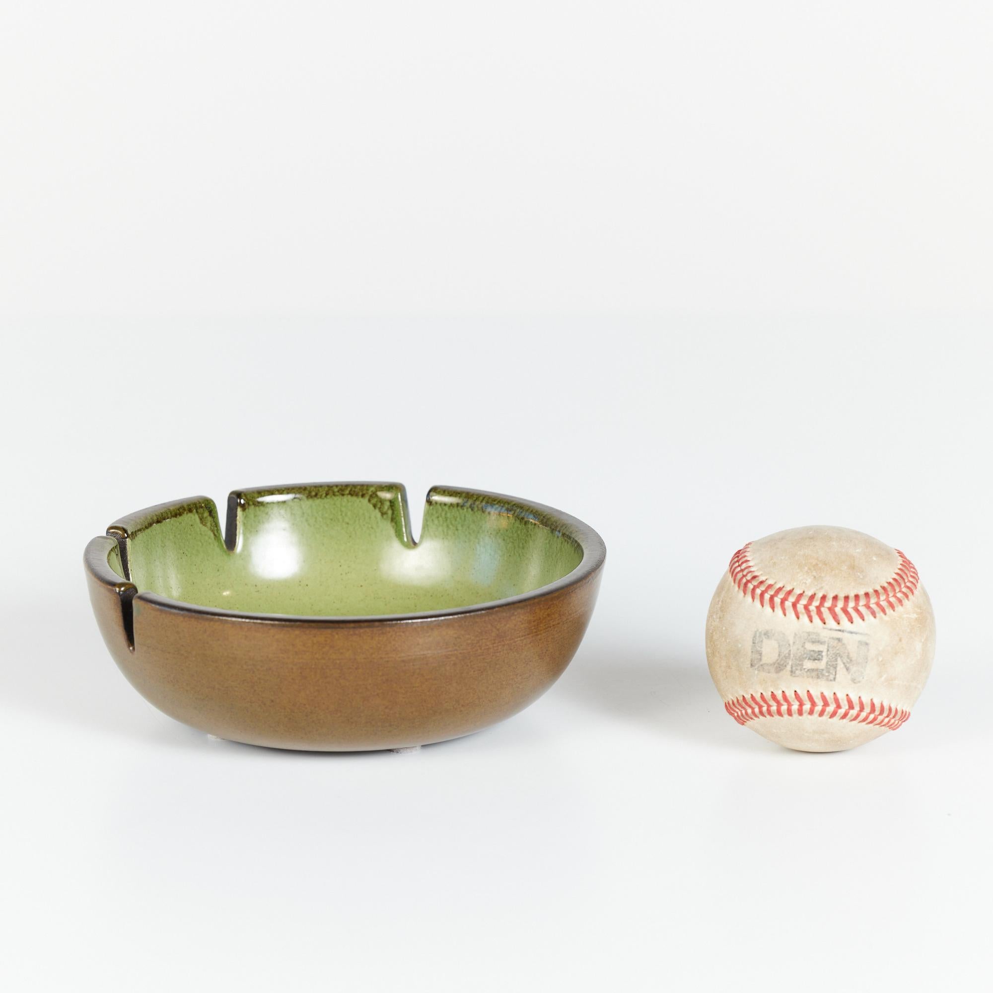Glazed ceramic ashtray by Heath Ceramics, c.1960s, USA. The ashtray features a dark green exterior glaze and light green speckle glazed interior. There are four holding slots for cigarettes. Can also be used as a decorative catchall or soap