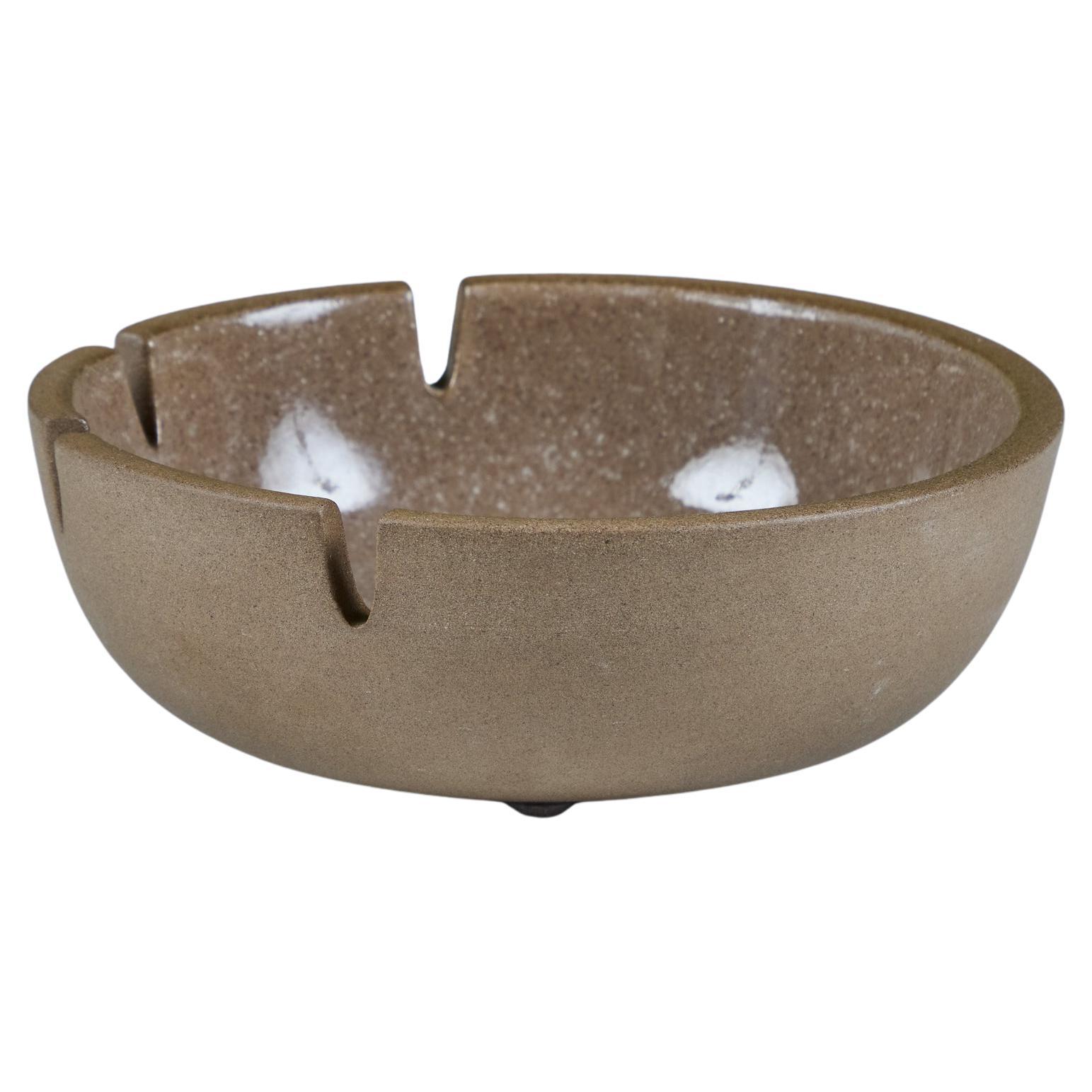 Ceramic ashtray by Heath Ceramics, c.1960s, USA. The ashtray features a stoneware exterior and tan speckle glazed interior with a purple glazed burst at the center of the well, with four divots at one curve. Can also be used as a decorative catchall
