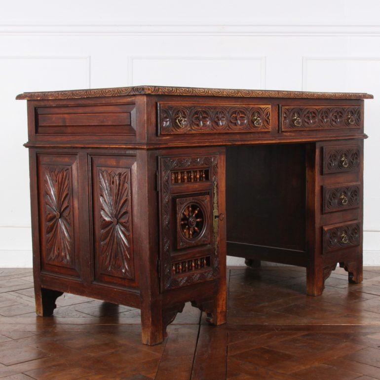 A late 19th century, French double-pedestal desk fitted with two upper drawers and three to one side, all with Gothic carved fronts. The left pedestal is a cabinet, the door with carved details and turned spindles. Carved raised panels to the sides
