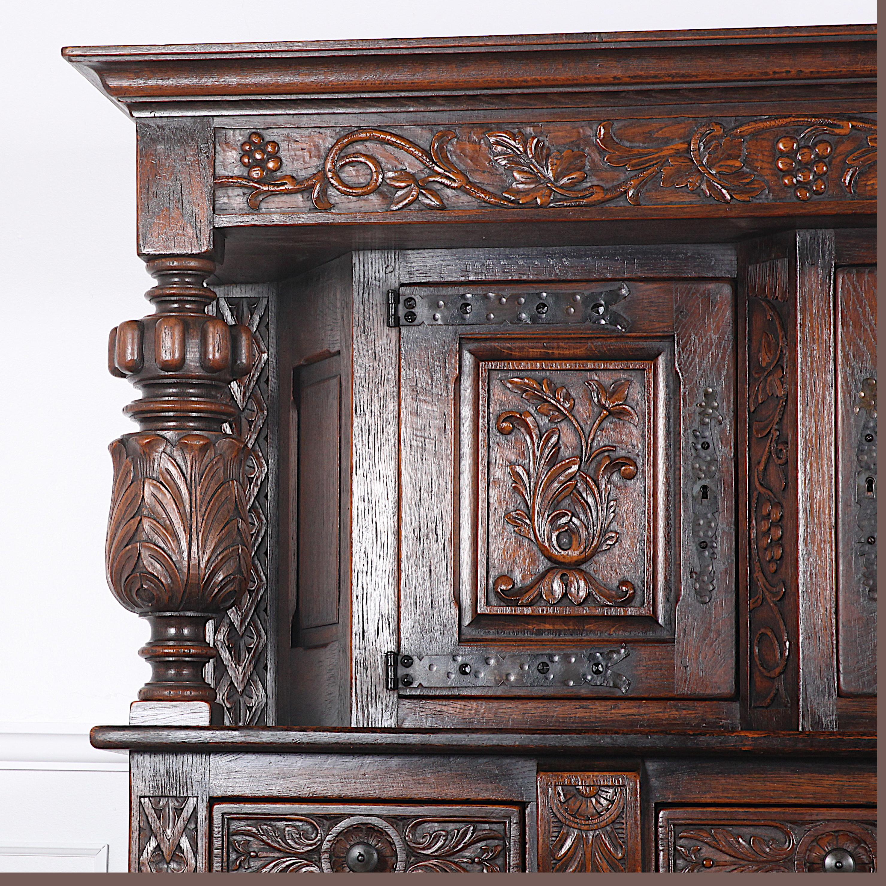  A heavily-carved solid oak Flemish court cupboard with three carved paneled upper doors over a lower cabinet with three drawers and two double-hinged carved cupboard doors. Large turned and carved columns flanking the top cabinets.
