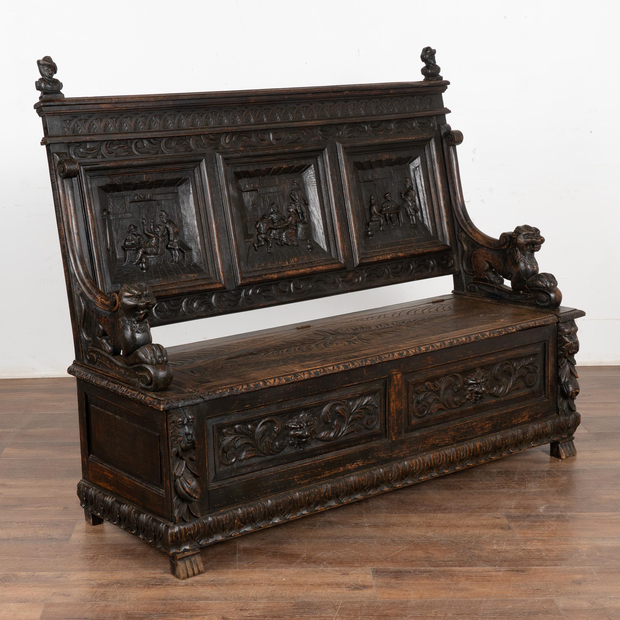 Highly carved oak high back bench. Three panels along the back portray pub scenes, while lions, heads, and carved flourishes are seen throughout the rest.
Notice the seat is hinged, creating great storage space for items that need to be discretely