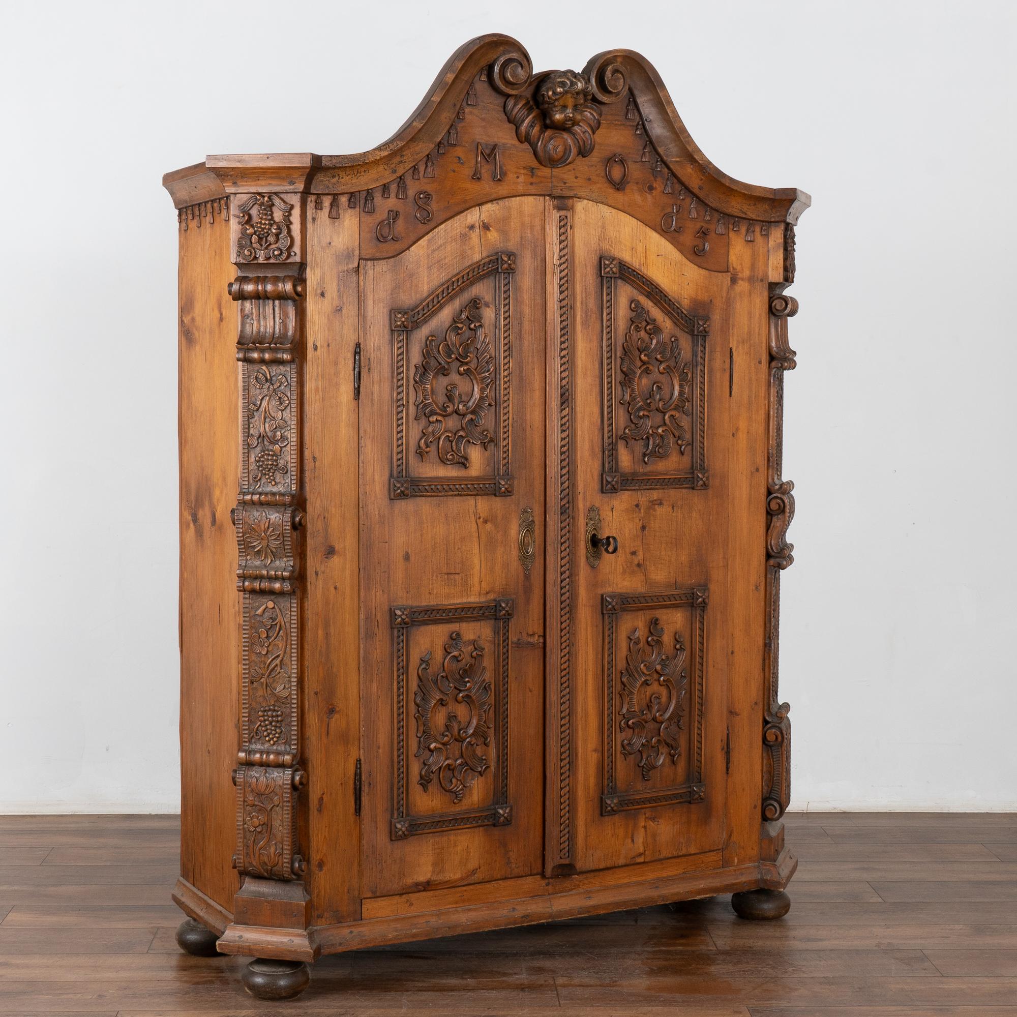 I dettagli intagliati a mano abbondano in questo piccolo armadio a due ante in legno di pino. Nota le nappe intagliate, il volto centrale del cherubino, i grappoli d'uva e le viti, le decorazioni e molto altro ancora in questo armadio.
La grande