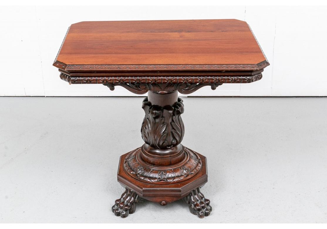 Heavily carved mahogany parlor table with rectangular form, having cantered corners, apron with carved acanthus leaves, the bold pedestal encircled with carved foliate motifs and surmounted on an octagonal base and raised on bold paw