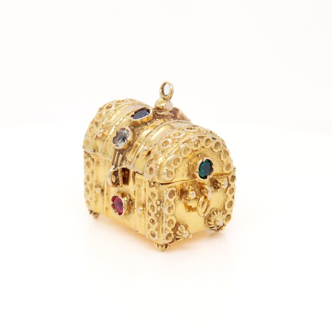 A very fine figural treasure chest charm.

In 14k gold.

In the form of an antique treasure chest with a hinged lid that opens, a snap front closure, and loop handles.

Bezel-set with round-cut white aquamarines, blue topazes, emeralds, and