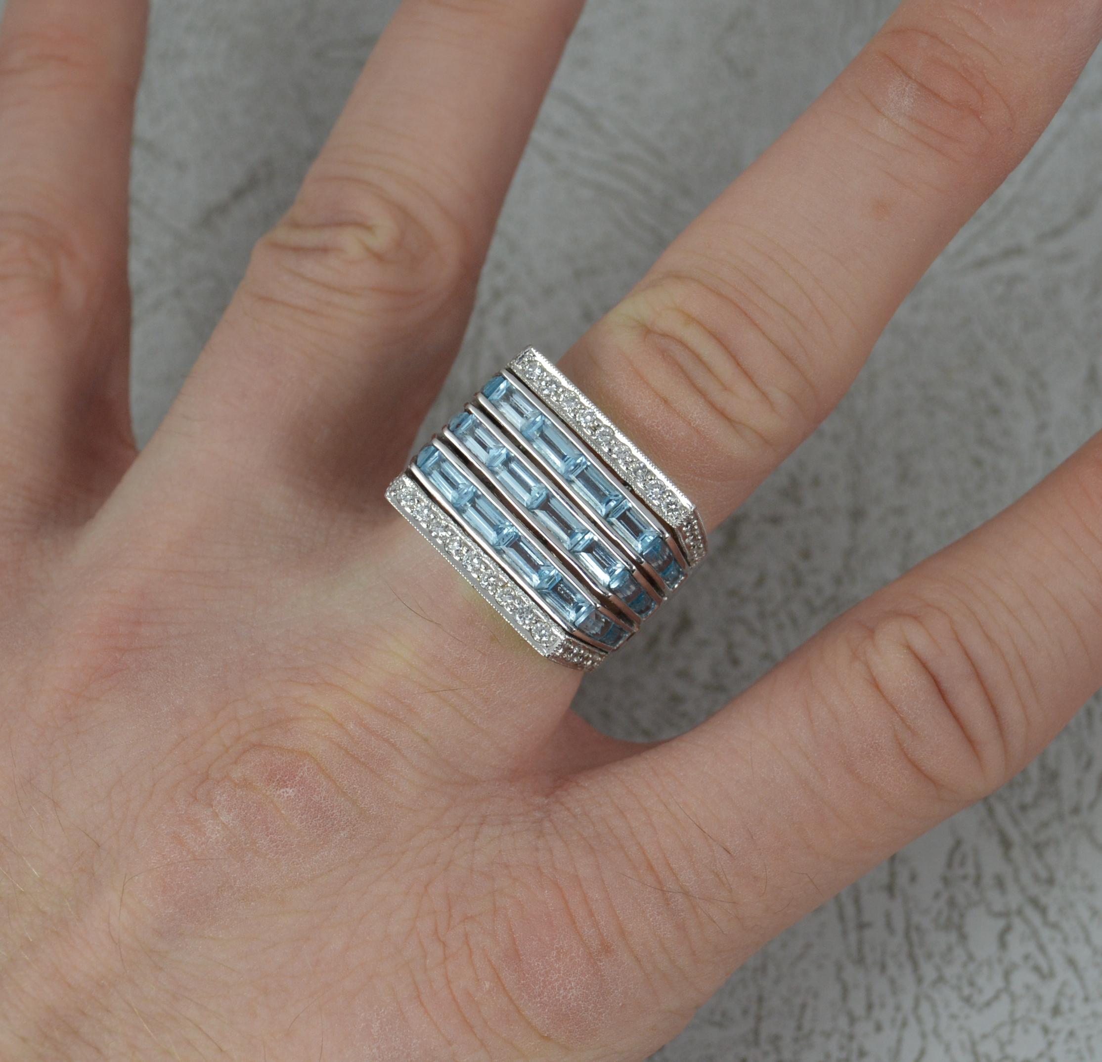 Ein schwerer Ring aus 18 Karat Gold, Topas und Diamanten.
Drei horizontale Reihen von blauen Topasen im Baguetteschliff mit weiteren Reihen von runden Diamanten im Brillantschliff oben und unten. 3.64 Karat Topas und 0,52 Karat Diamanten.
18mm x