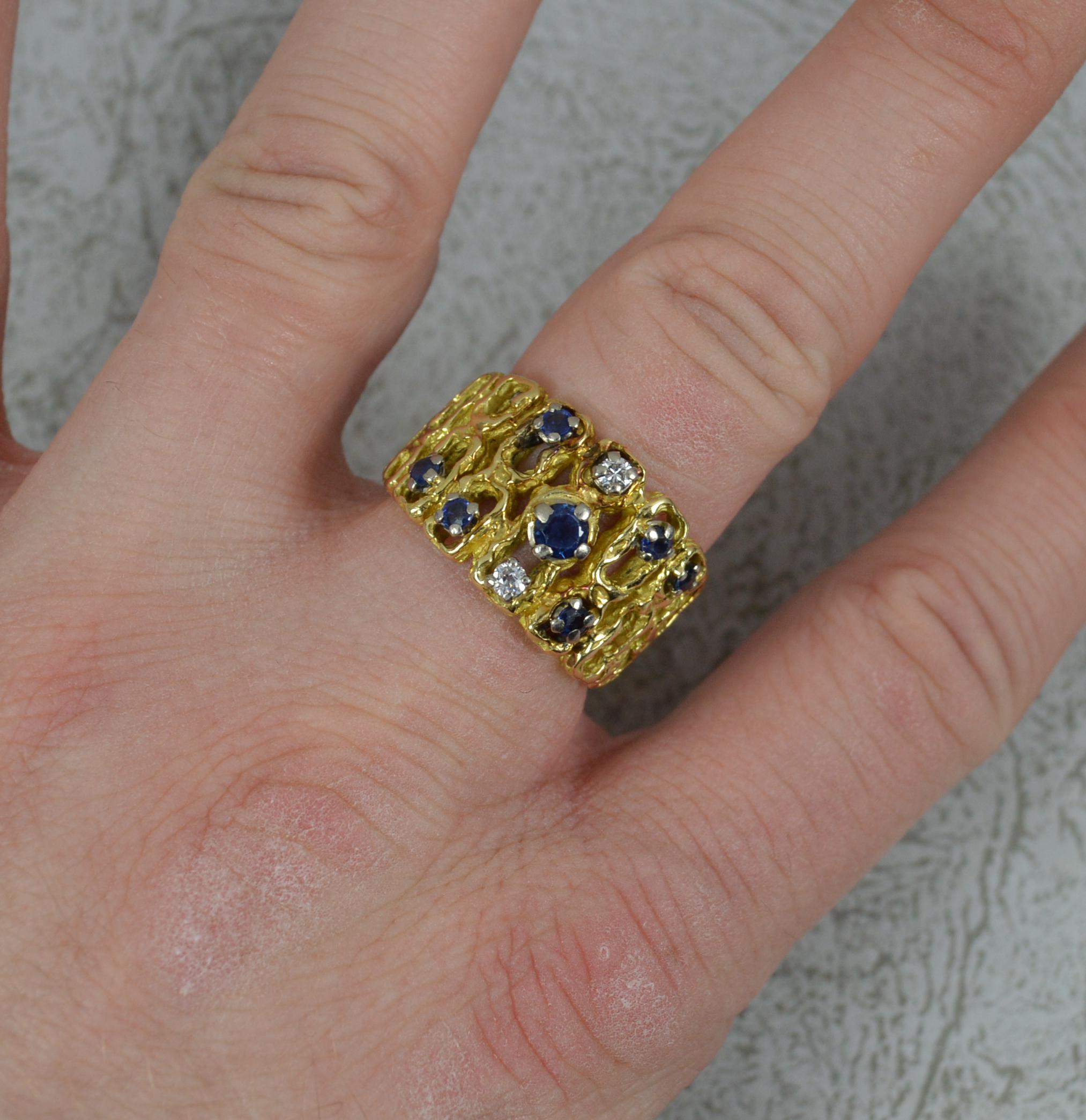 A superb quality abstract design cluster ring. c1970.
Solid 18 carat yellow gold example with a unique pattern throughout the band.
Designed with seven dark blue, round cut sapphires and two round cut diamonds. 
14mm wide band to the