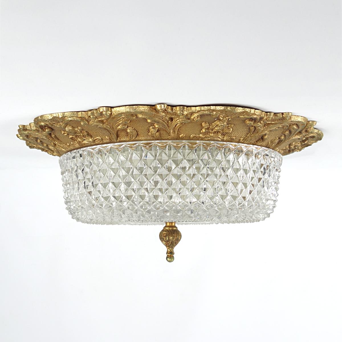Classic heavily detailed flush mount made of brass and glass. 
The fixture is casted in a French lily motif and the heavy glass shade is cut in a geometric pattern. This causes many planes that cut the light ensuring for a very sparkling effect. A