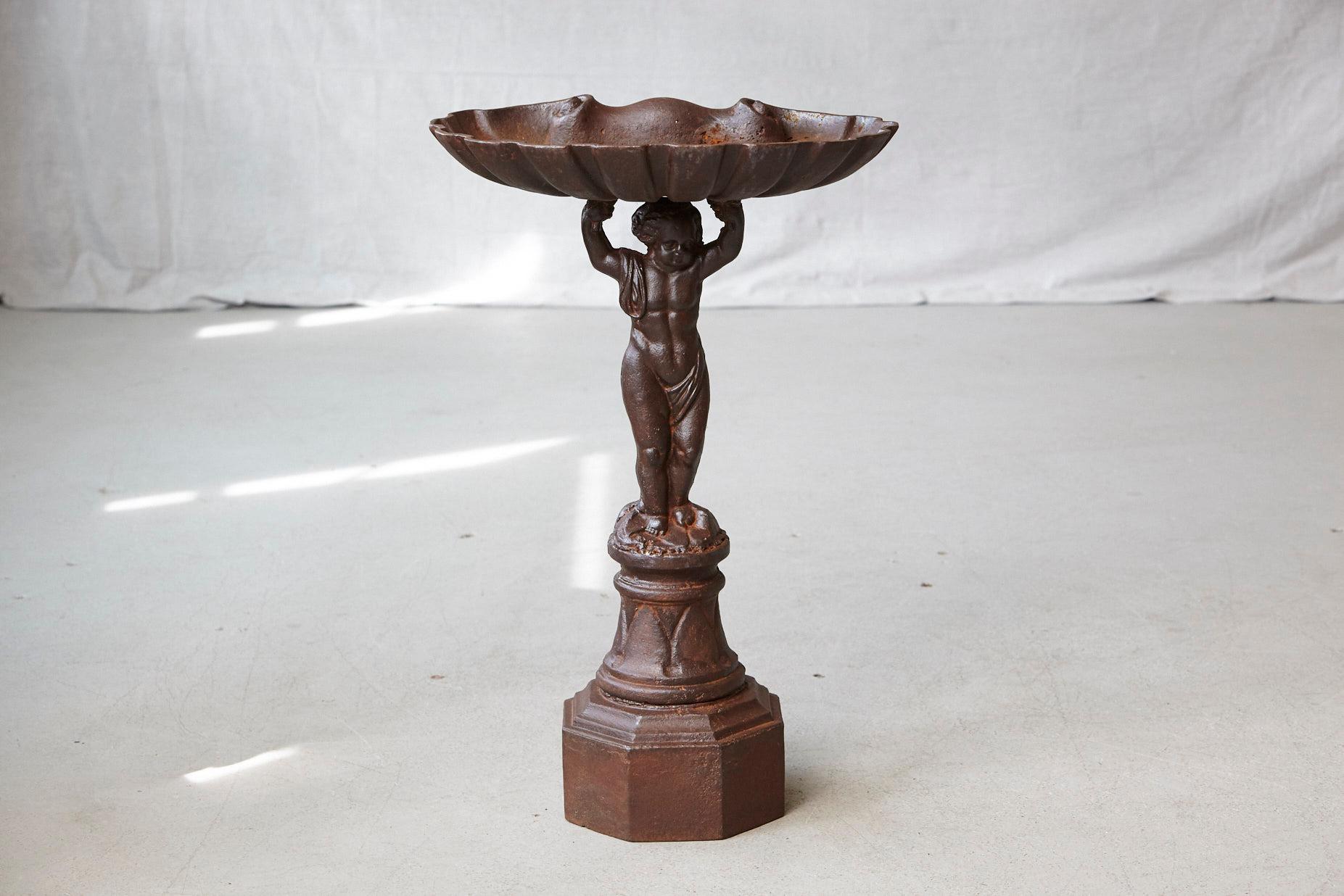 A gorgeous, heavy, cast iron birdbath, showing standing putti with raised arms holding a large shell above his head, mounted on an octagonal base, circa 1900s
Fantastic patina and colors.