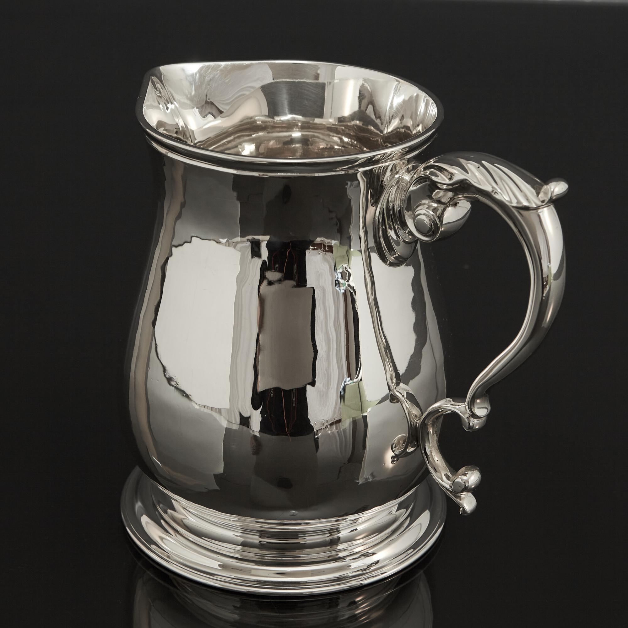 Pleasingly simple style of silver water jug of bellied, pear-shaped form, fitted with a scroll and acanthus leaf pattern handle. The body is mounted on a spreading circular base. This wonderful quality piece is made from hand-raised silver and the