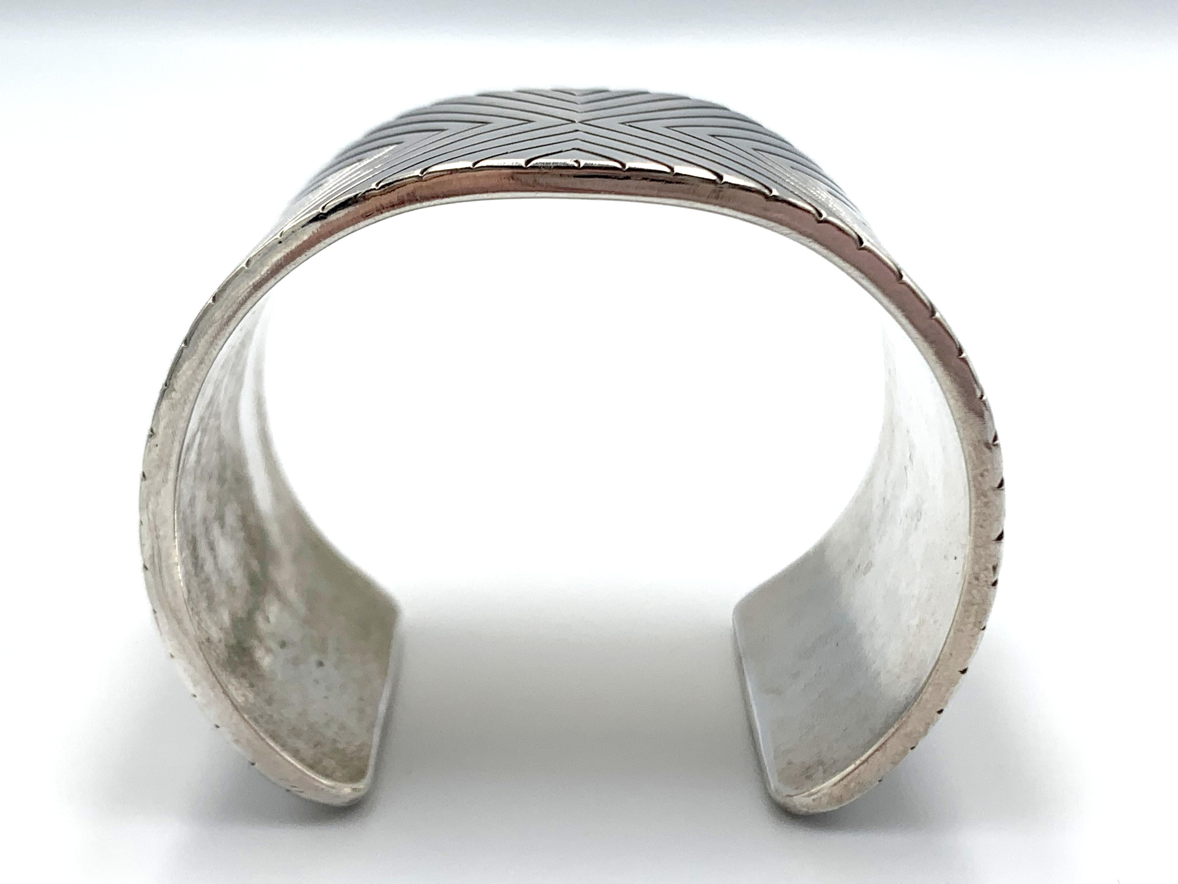 Questo braccialetto di grande effetto, realizzato a mano dal famoso argentiere Navajo Matthew Charley, è realizzato in argento sterling di grosso calibro. La fascia ampia e sostanziosa presenta disegni geometrici intagliati a mano, con un motivo