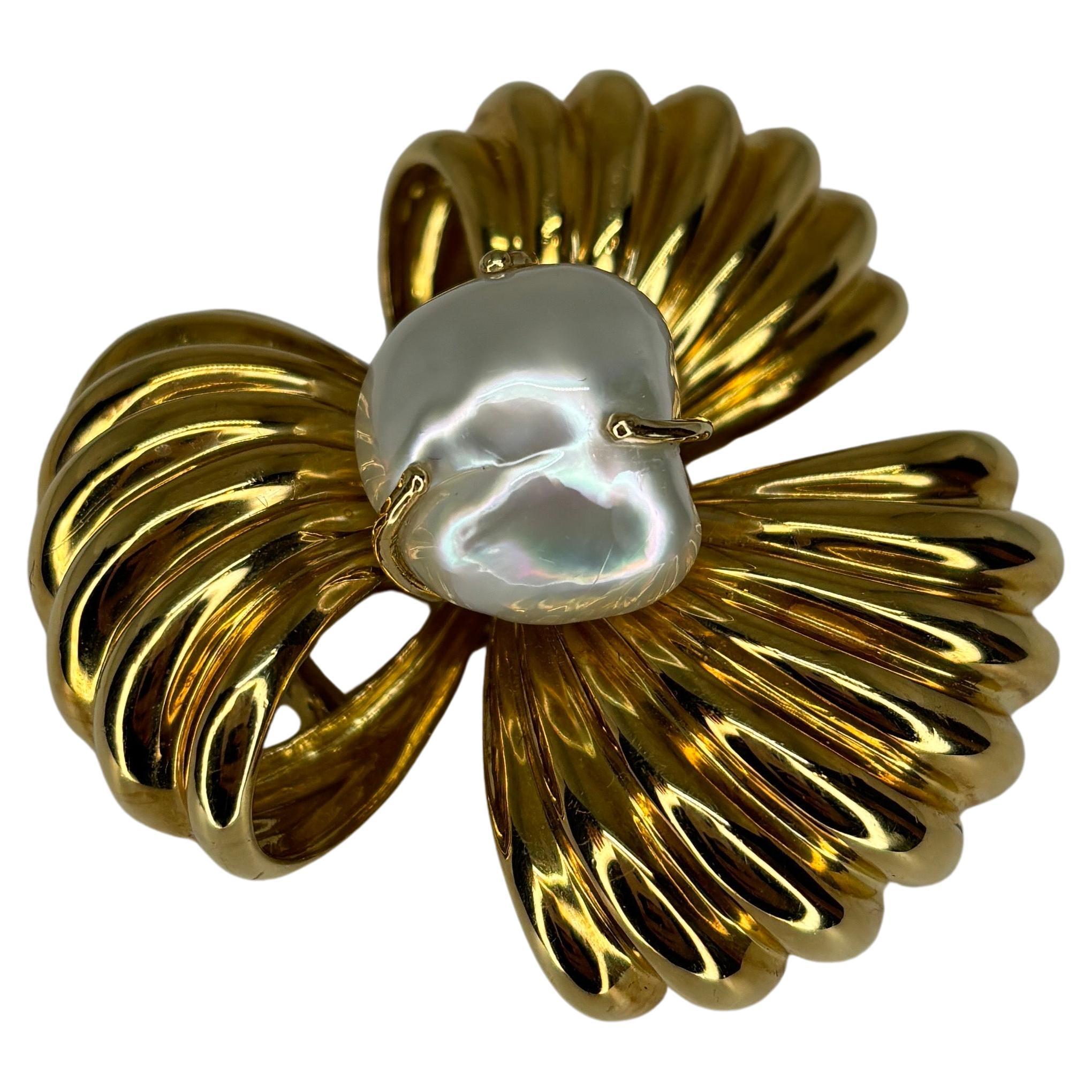 Luxurious large brooch featuring a large white baroque pearl at the center of ribbed looped ribbons of 18k yellow gold.

Baroque pearls are known for their irregular, non-spherical shapes, which give them a distinct and often dramatic appearance.