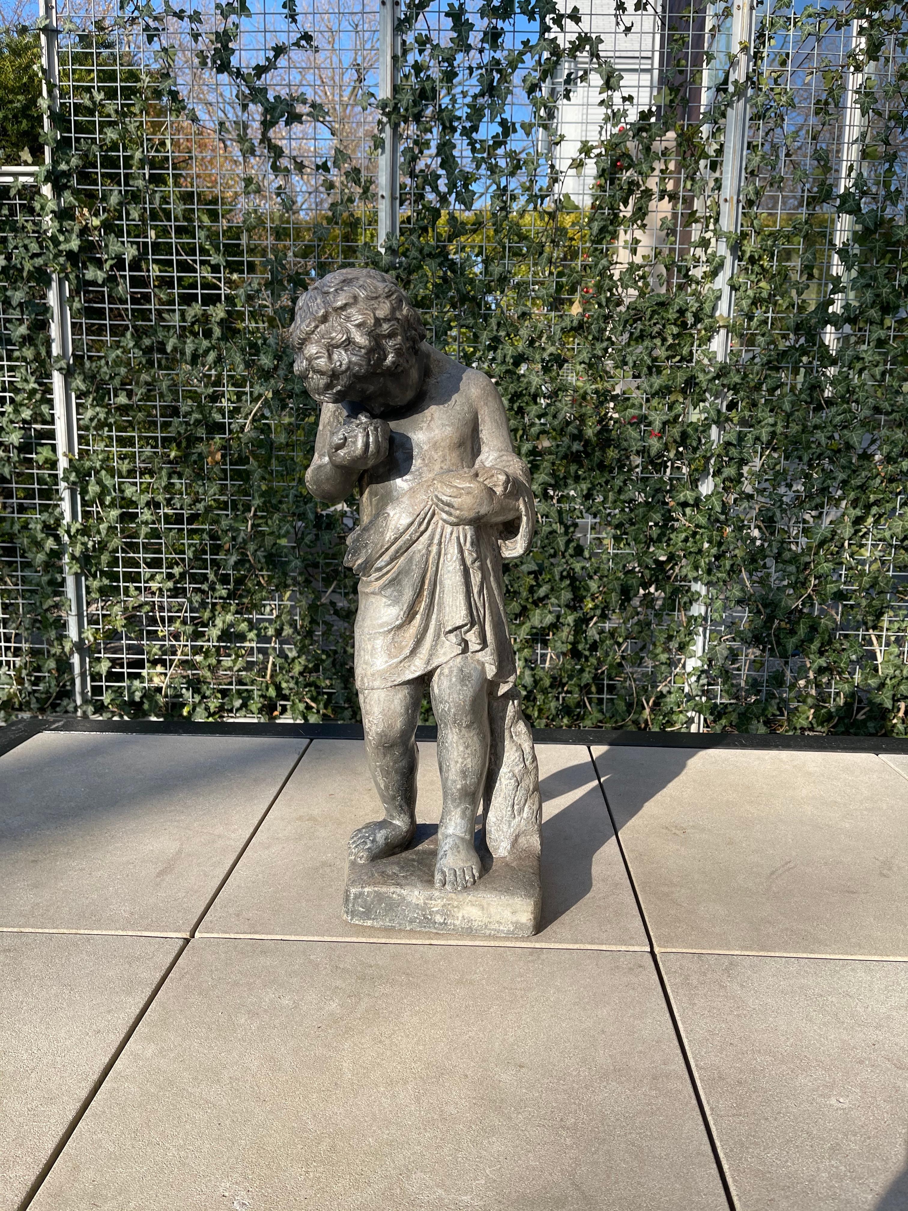 Lead putto statue depicting an Italian curly haired young boy, with animal skin around his waist and draped over his forearm. He gazes closely at a nest with two baby birds that he holds gently in his right hand. He stands at 24.75
