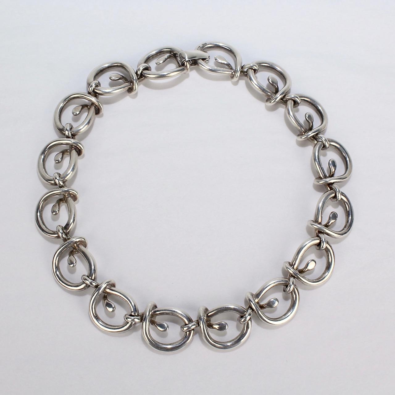 A stylish heavy gauge dog collar or choker necklace by Tane.

With wide-looped links and a snap-lock clasp. 

The collar is thick and has substantial heft. A true pleasure to wear! Simply high quality silversmithing from the top-shelf Mexican house