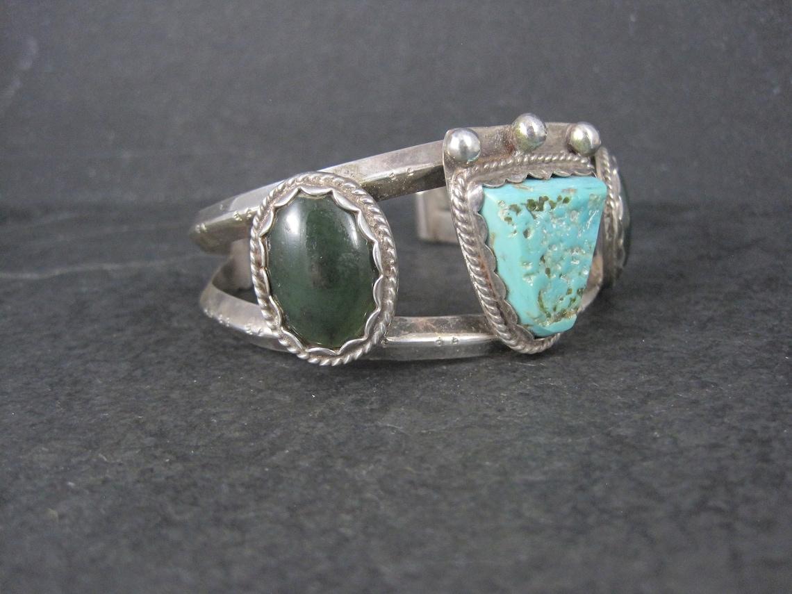 This gorgeous, unique 1970s cuff bracelet is sterling silver with turquoise and jade gemstones.

The face of this cuff measures 1 1/8 inches wide.
It has an inner circumference of 6 1/4 inches including the 1 1/4 inch gap.
Weight: 42.7 grams

Marks:
