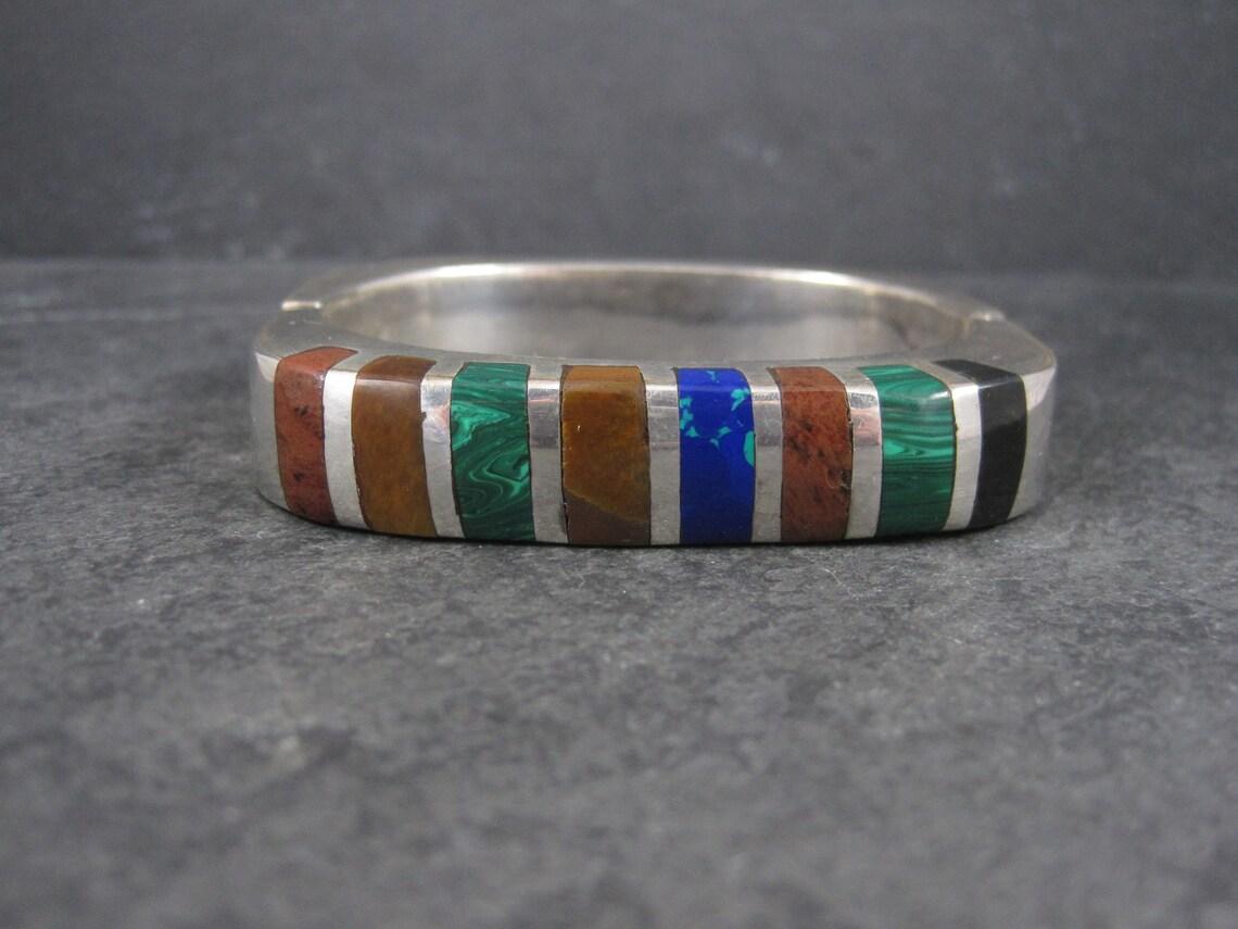 This gorgeous Mexican bangle bracelet is sterling silver.
It features onyx, malachite, jasper, azurite and tiger eye inlay.

This bracelet measures 1/2 of an inch wide.
It has an inner circumference of 6 1/4 inches.
The inner diameter measures 1 3/4