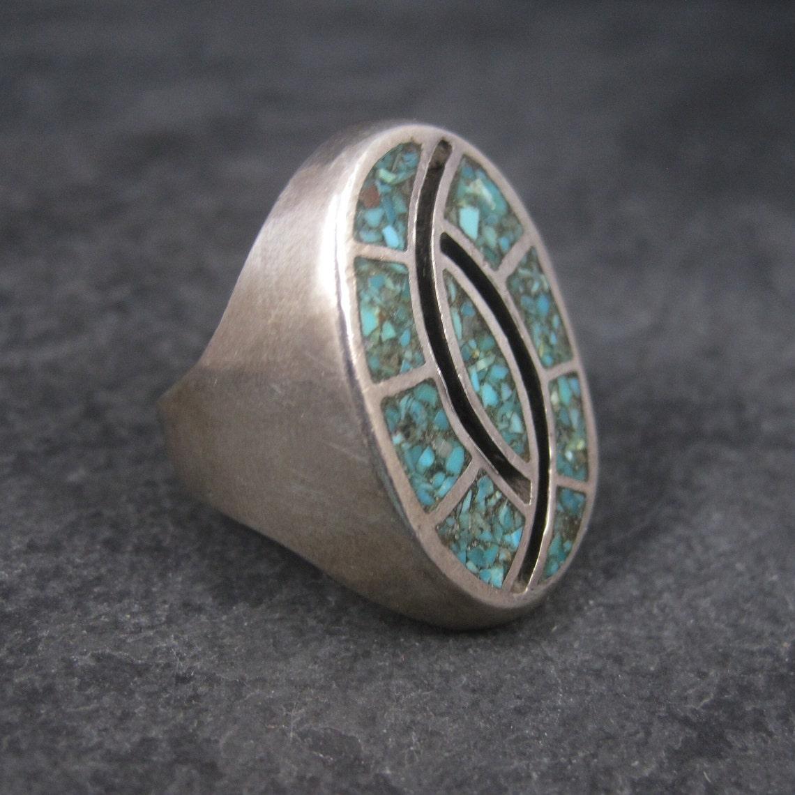 This beautiful 1970s southwestern ring is sterling silver.
It features turquoise chip inlay.

The face of this ring measures 1 3/16 inches north to south.
Weight: 23.3 grams
Size: 9.5

Marks: None 

Condition: Excellent
