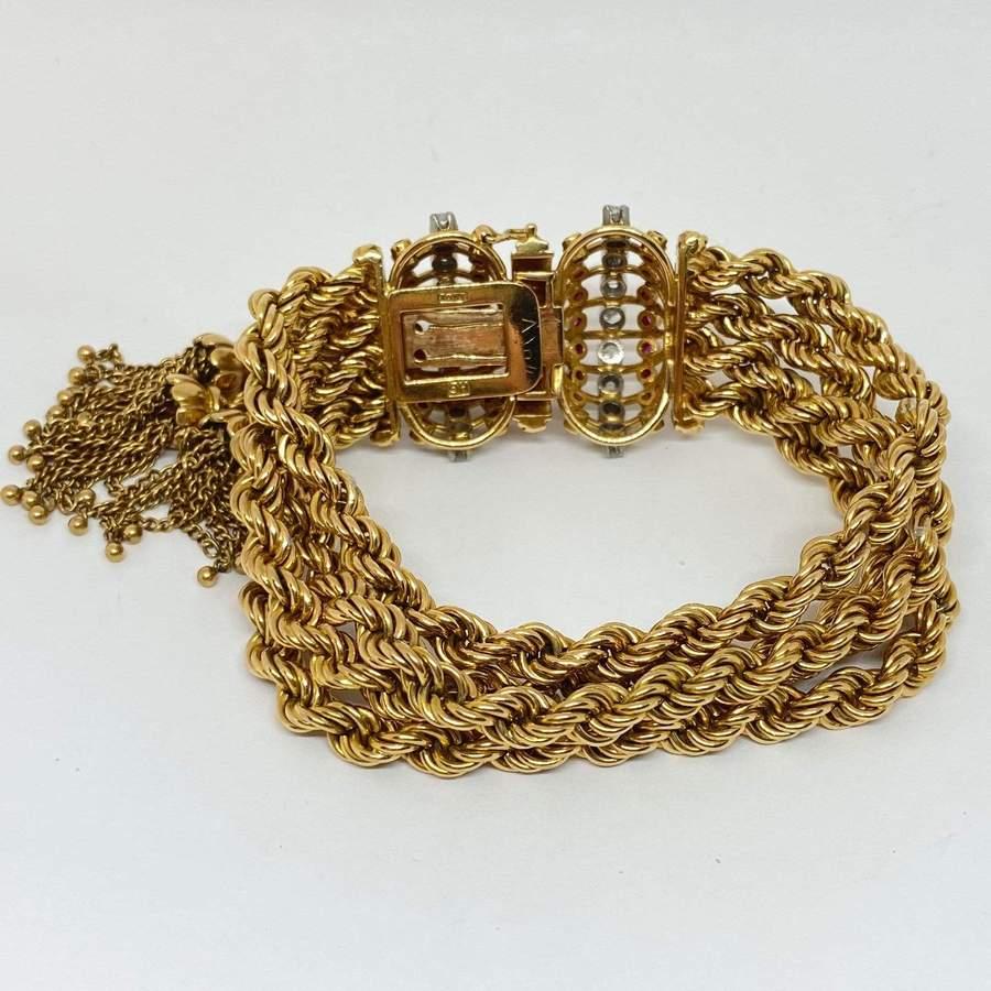 Estate diamond & ruby rope and tassel bracelet designed in 18 karat yellow gold.  Four (4) loose rope chains are connected to decorated clasp ends. It contains round brilliant cut diamonds and round faceted rubies. Wide tongue and box clasp.