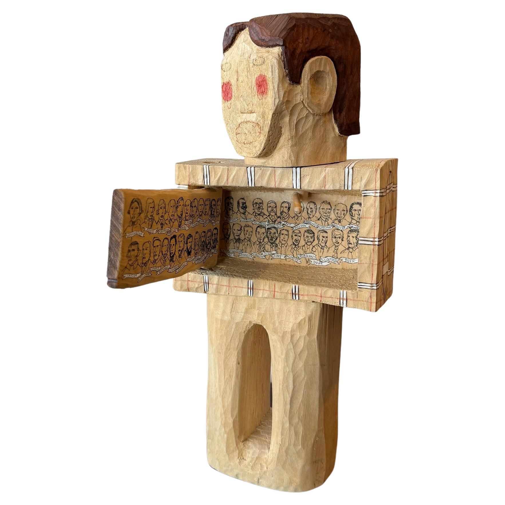 Handgeschnitzte Lindenholzskulptur des zeitgenössischen Künstlers Hector Ruiz, die eine männliche Figur mit einer sich öffnenden Tür im Brustbereich darstellt. Die Arbeit reflektiert darüber, wie die USA vor der Wahl Obamas 40 weiße Männer als