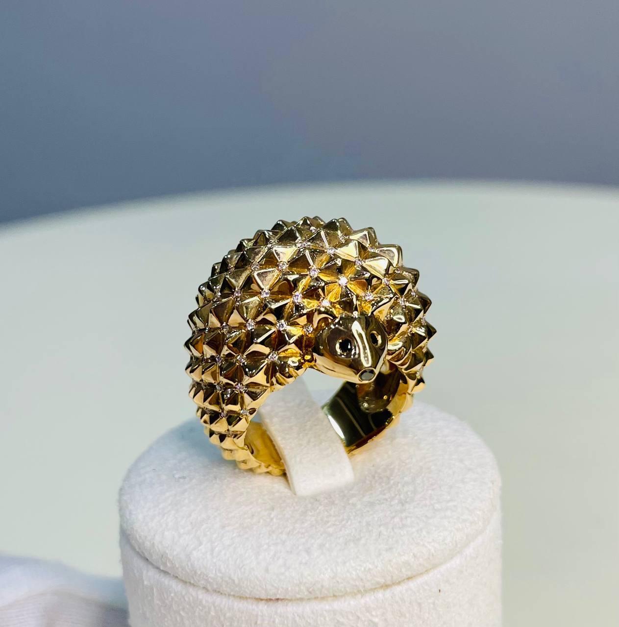 Gold Hedgehog Ring. This unique ring is crafted in gold, featuring a detailed hedgehog design with a textured, spiky surface. The intricate craftsmanship highlights the hedgehog's face and body, creating a striking and whimsical piece. The ring is