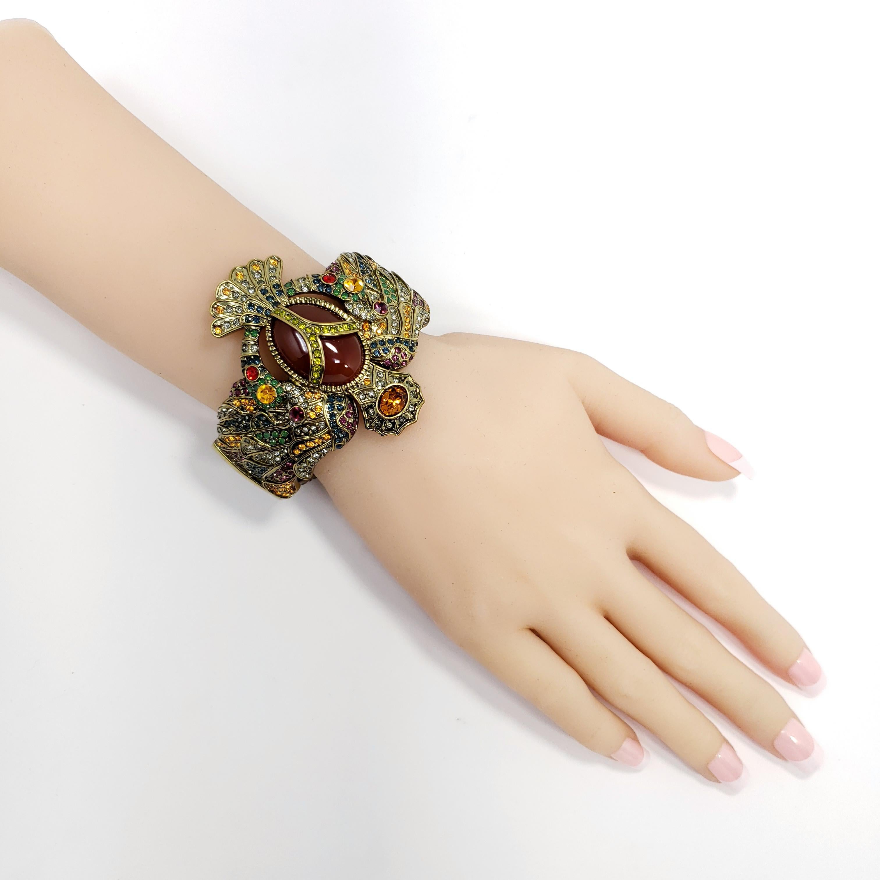 This Egyptian inspired cuff bracelet looks like it came from the tombs of Egypt. The oval cuff silhouette depicts a winged Egyptian scarab. A large oval carnelian cabochon is bezel-set in the center and cradled by a pave crystal-lined, Y-shaped
