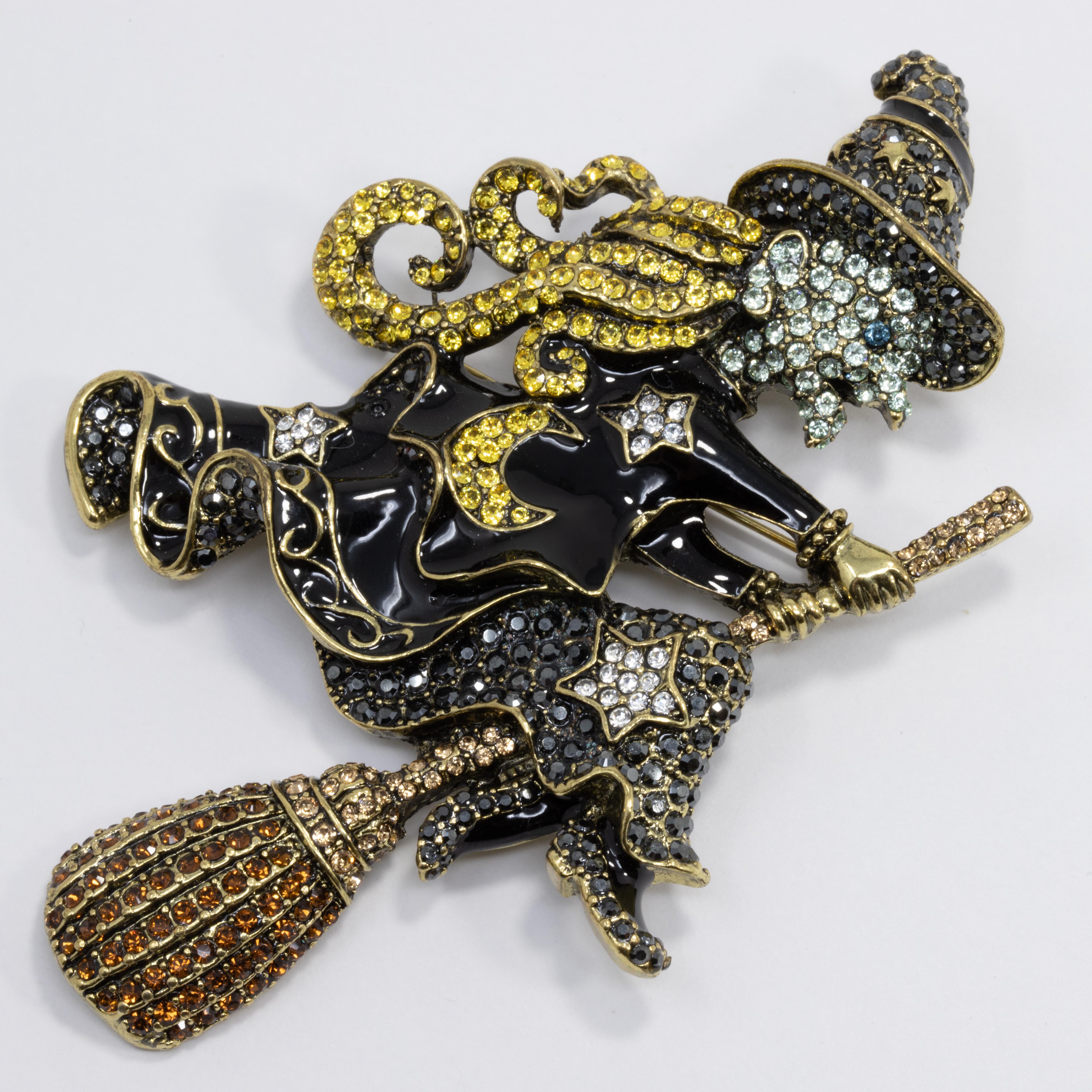 A whimsical pin by Heidi Daus. This lovely brooch features a witch on a broom, decorated with colorful pave crystals and painted with black enamel. Set on matching brass tone metal.

Hallmarks: Heidi Daus, CN