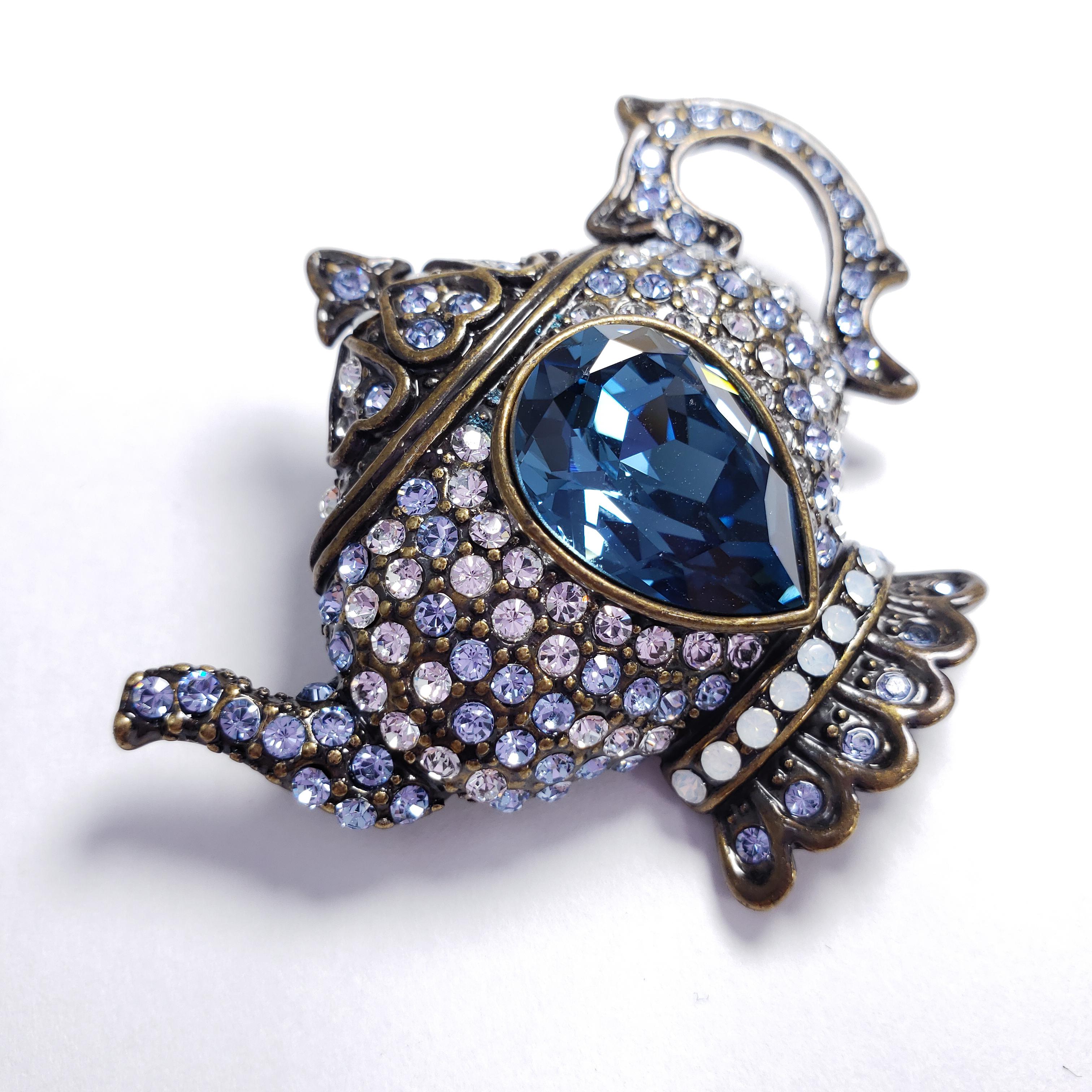 A whimsical pin brooch, featuring a teapot decorated with clear and blue pave crystals, along with a large centerpiece pear-cut blue crystal. By Heidi Daus.

Hallmarks: Heidi Daus, China
Originally made by Heidi Daus for her exclusive HSN line