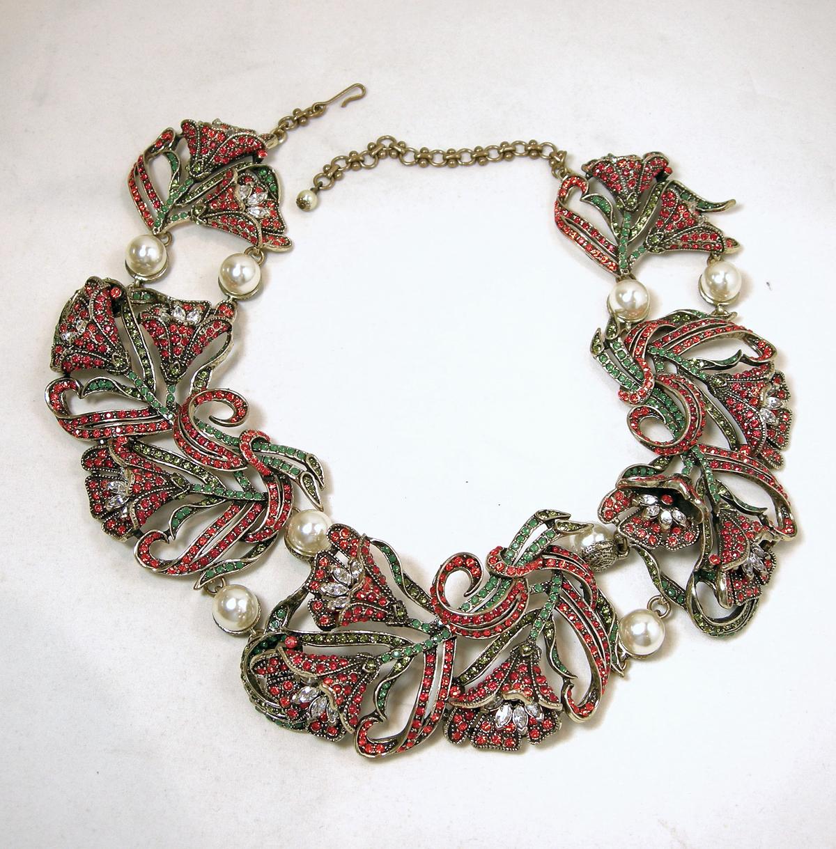 This signed Heidi Daus necklace has a 3-dimensional floral design with red, green & clear crystals. There are two faux pearls in-between the floral links.  It is in a gold tone setting with a hook clasp. This necklace is signed “Heidi Daus” and