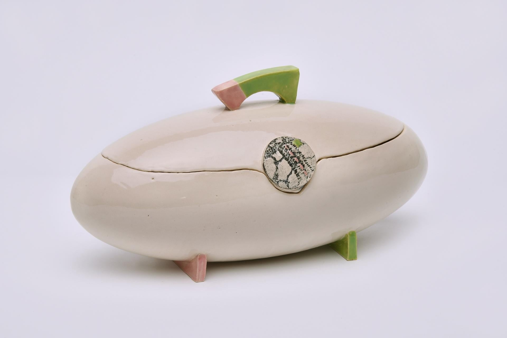 Esta elegante urna de cerámica hecha a mano con una suave forma ovalada, delicados soportes de suaves tonos verdes y rosas con finos detalles decorativos, mezcla diseño atemporal e inspiración natural. Este recuerdo es una pieza única elaborada con