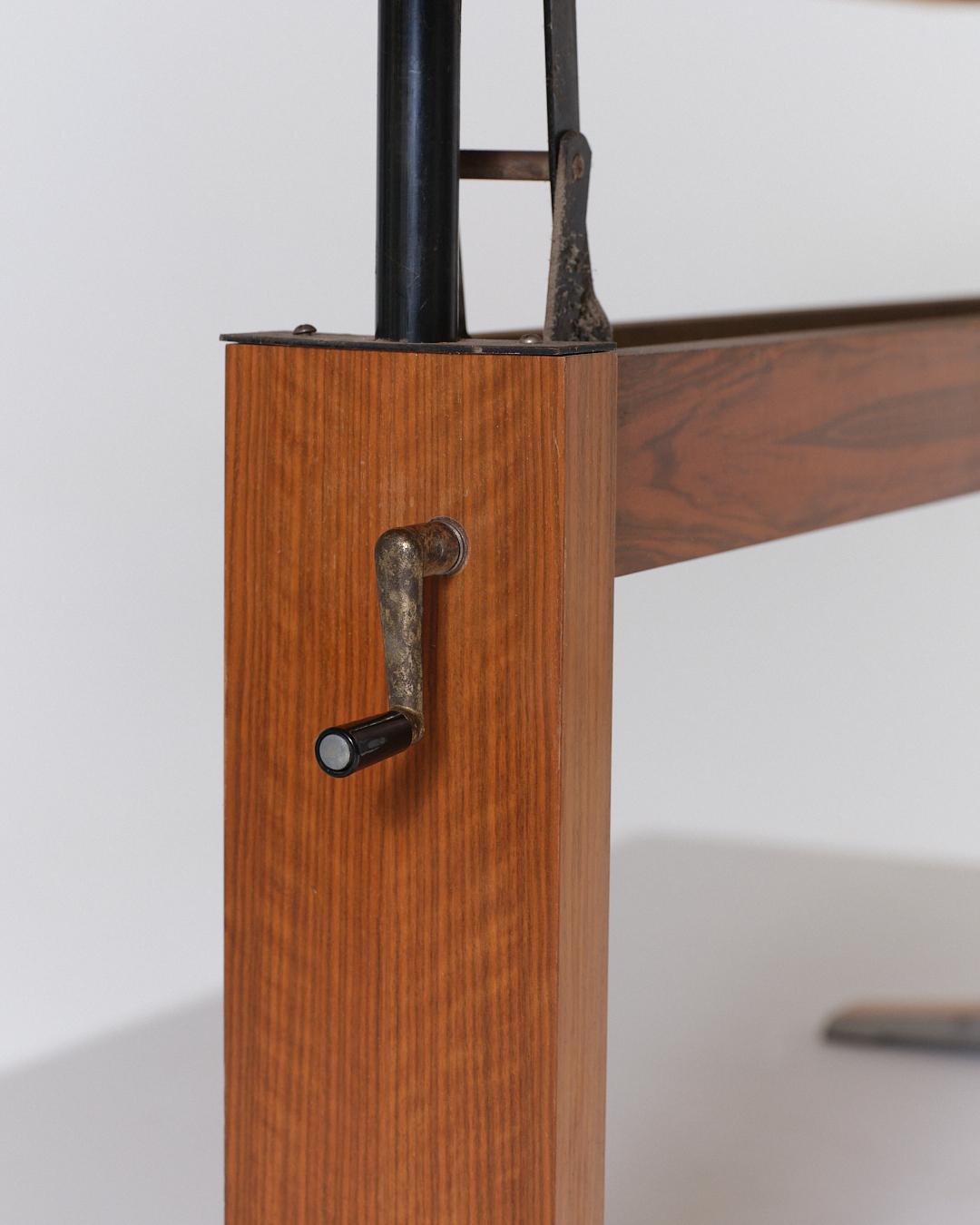 Table à manger réhaussable des années 1970, en bois avec un piètement contour métallique. Plateau réglable en hauteur par manivelle (jusqu’à 72 cm), pouvant aussi servir de grande table basse. Bon état général, un petit choc sur un angle du plateau.