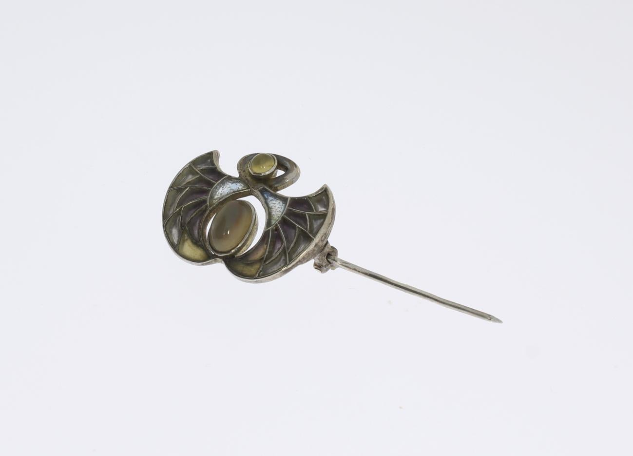 The brooch was made by Heinrich Levinger in Pforzheim, Germany, around 1902. Stylized wings form with plique-a-jour enamel decoration and 2 cabochon stones. Mounted in Silver. Marked on the back with DEPOSE STERLING. 
Weight: 4,55 g. Measurements